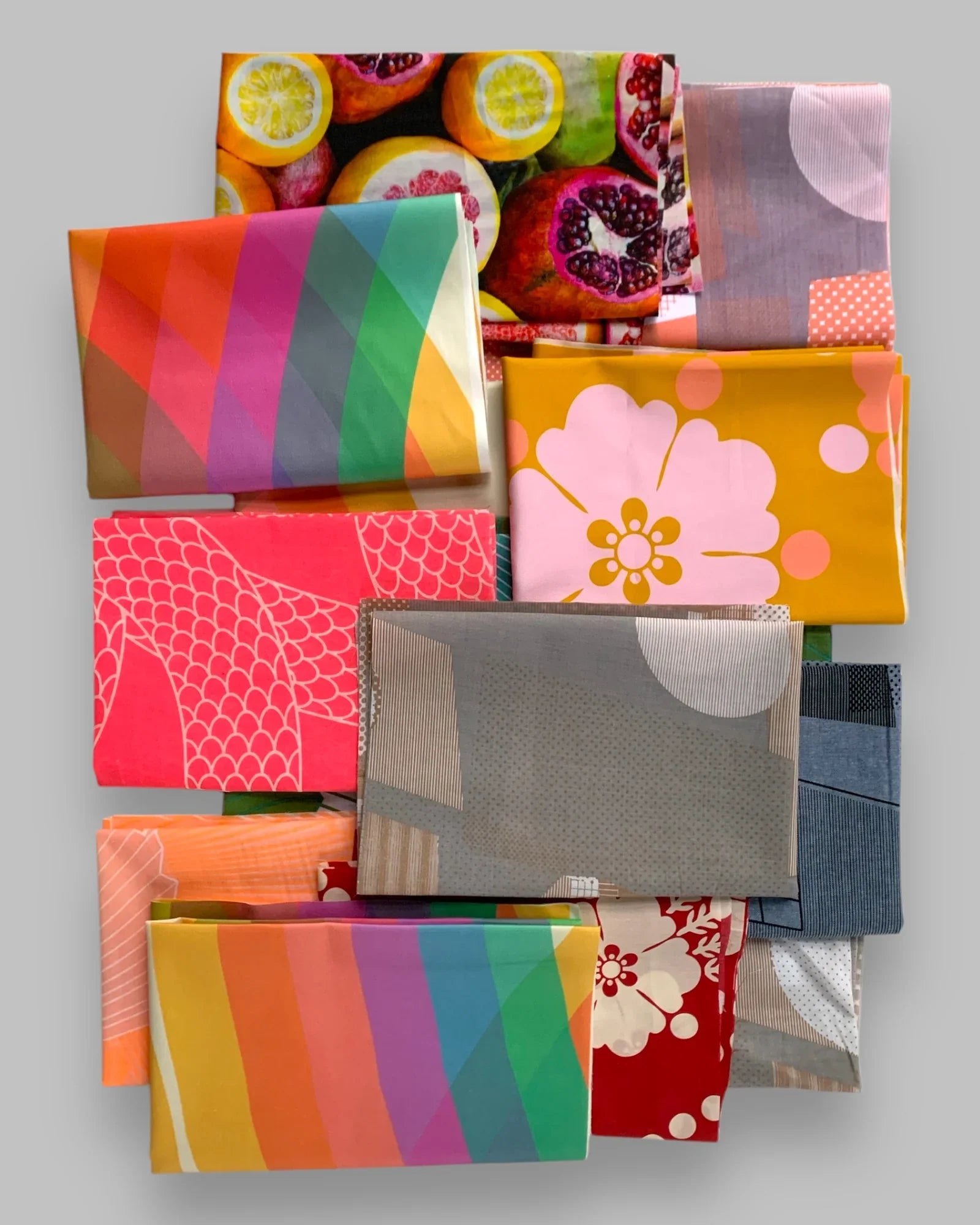 Stacked fat quarters with colorful Hawaiian and floral prints on a gray background
