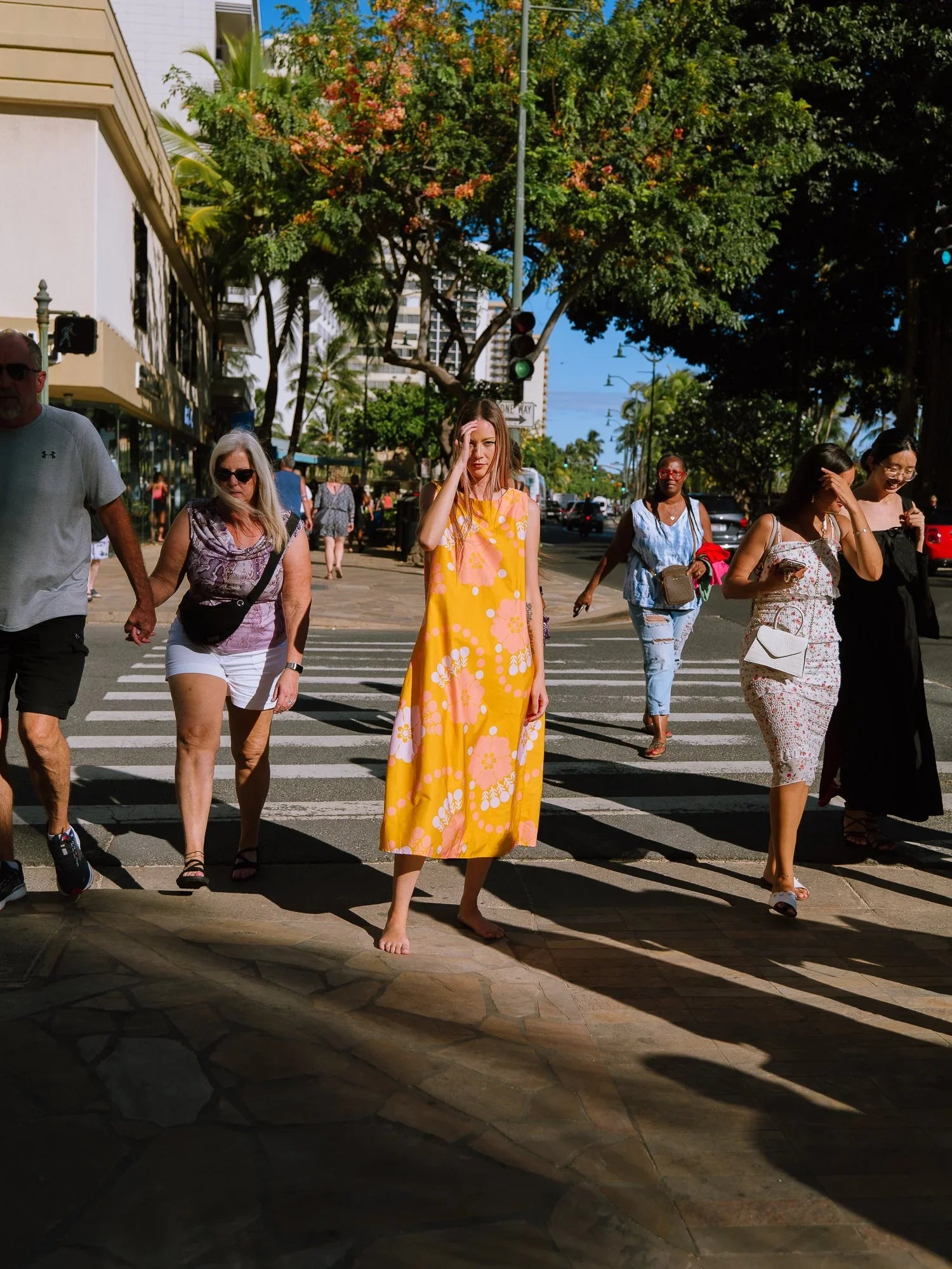 Woman in a yellow modern mu'umu'u dress with floral Hawaiian print crossing a city street