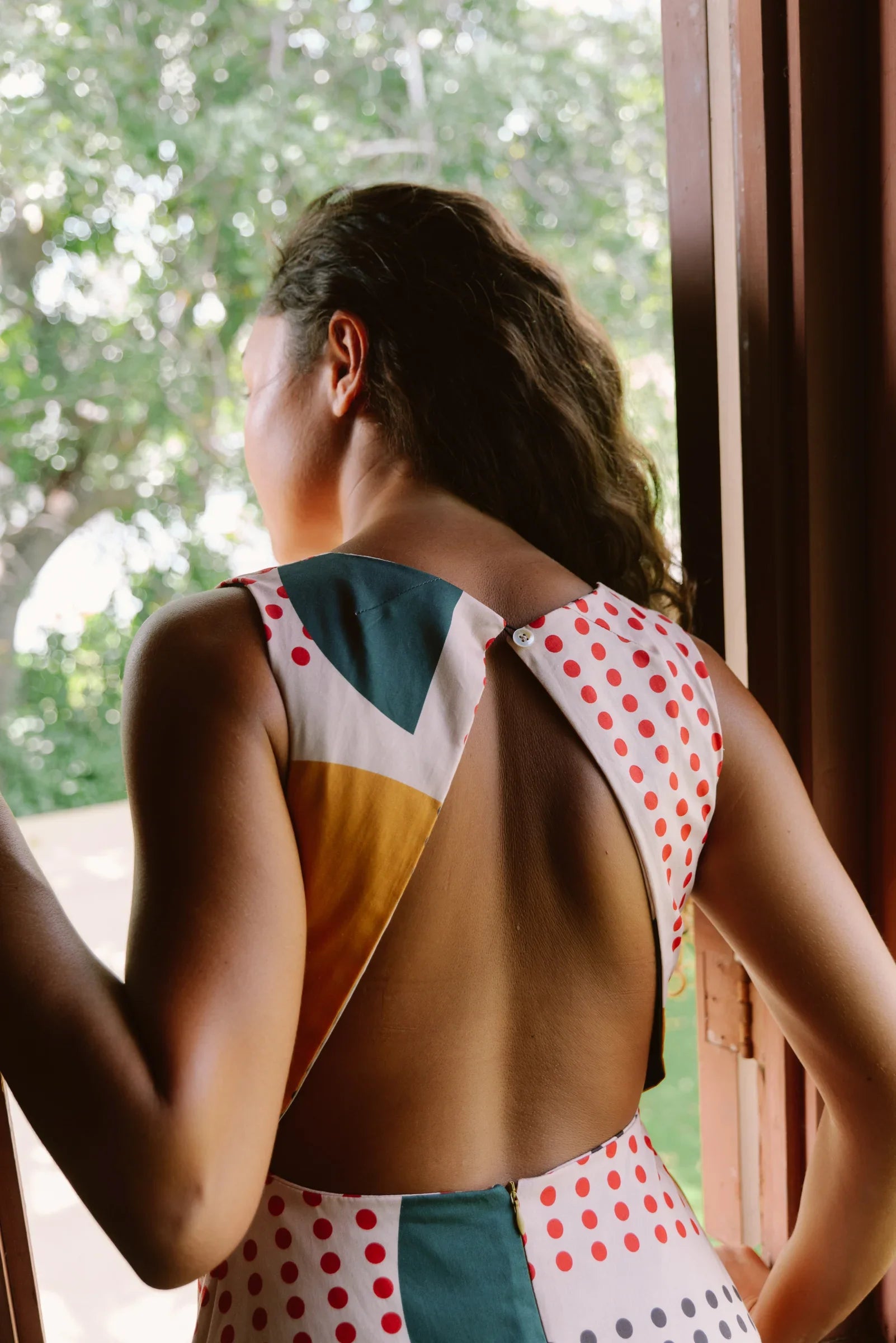 Woman in open-back modern mu'umu'u dress with colorful Hawaiian print by a window