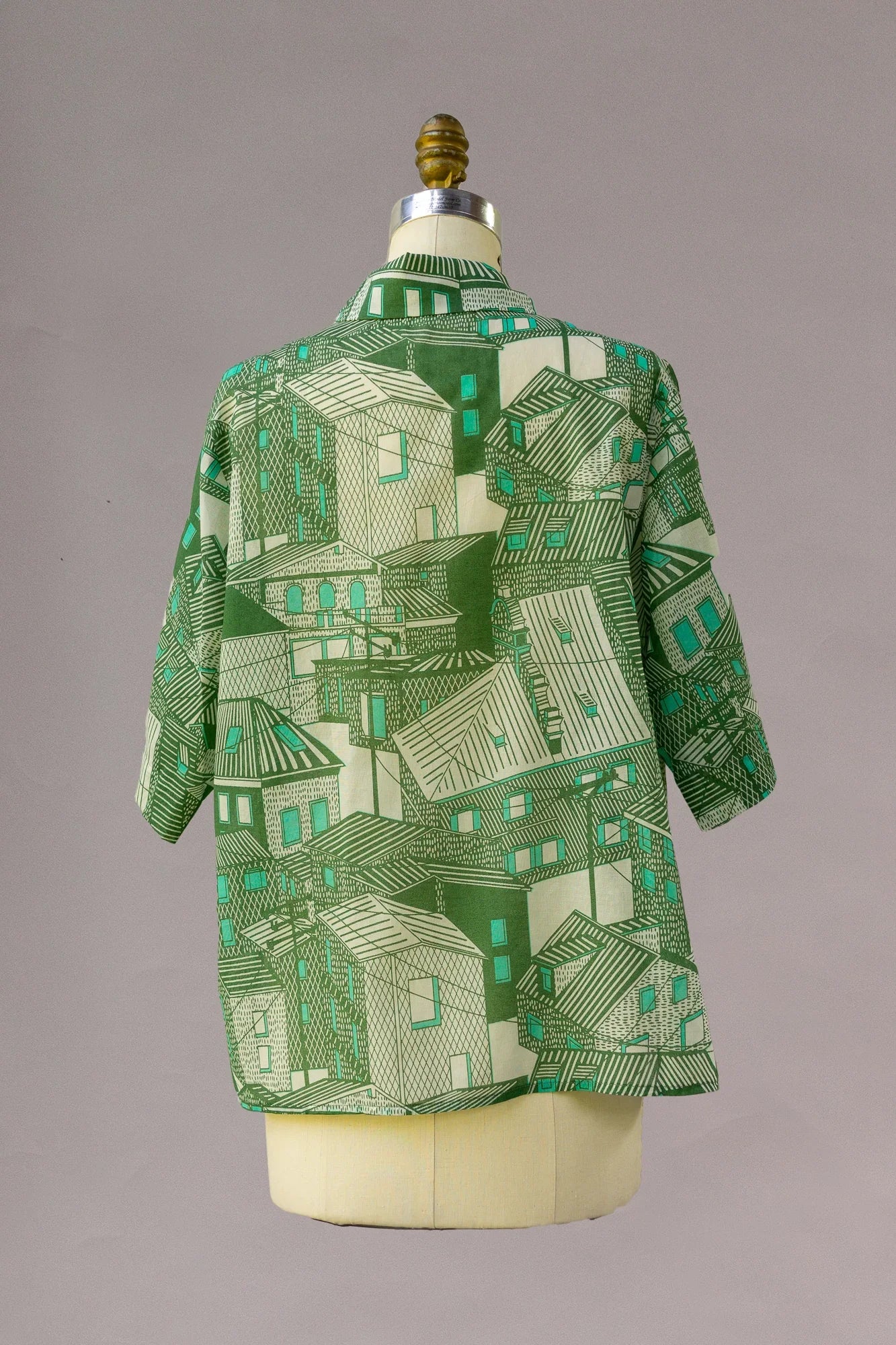 Green aloha shirt with geometric cityscape print, shown on a mannequin from the back.