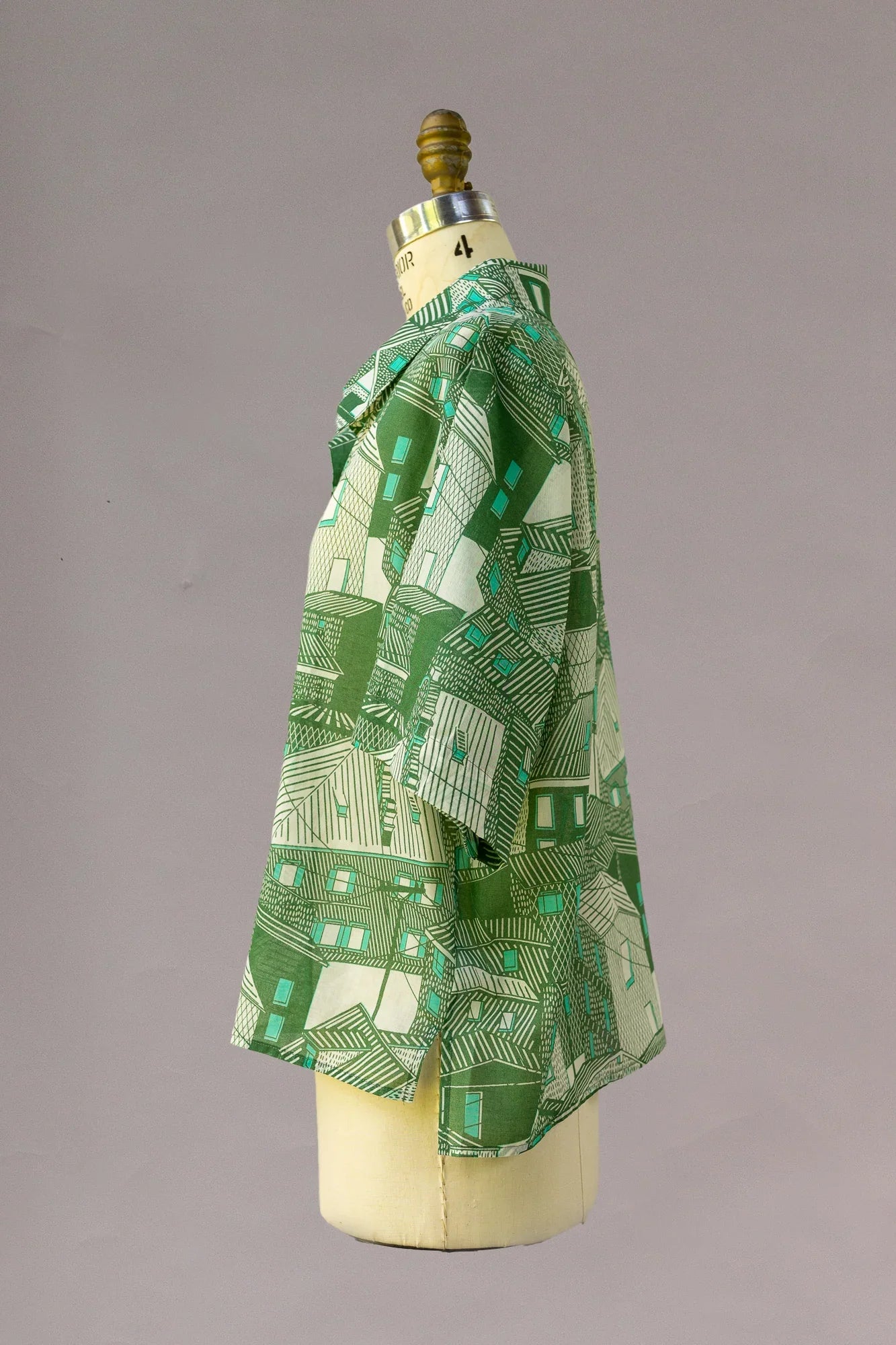 Green aloha shirt with geometric Hawaiian house pattern on dress form, side view