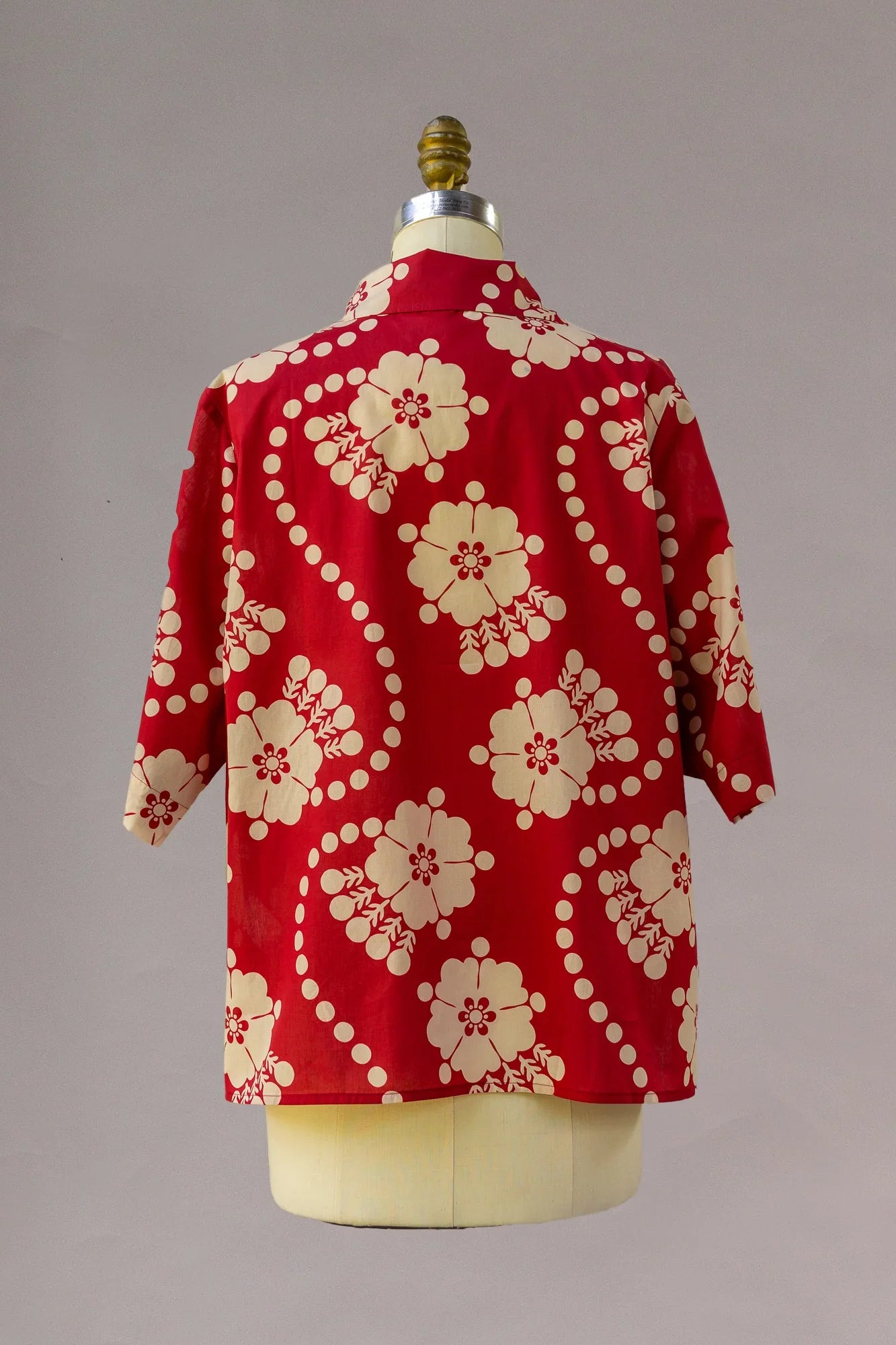Red aloha shirt with cream floral and dotted Hawaiian print, displayed on mannequin