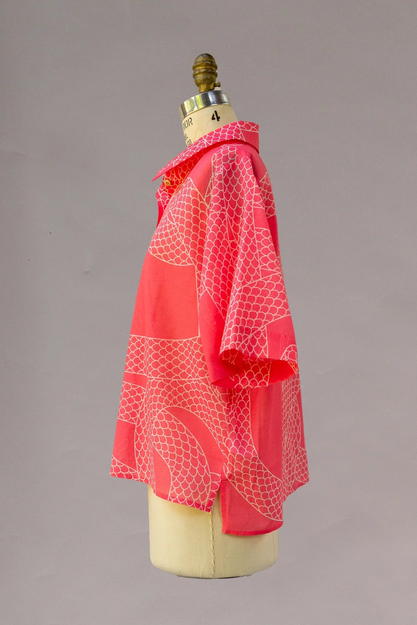 Side view of a red Hawaiian aloha shirt with white scale print on a dress form