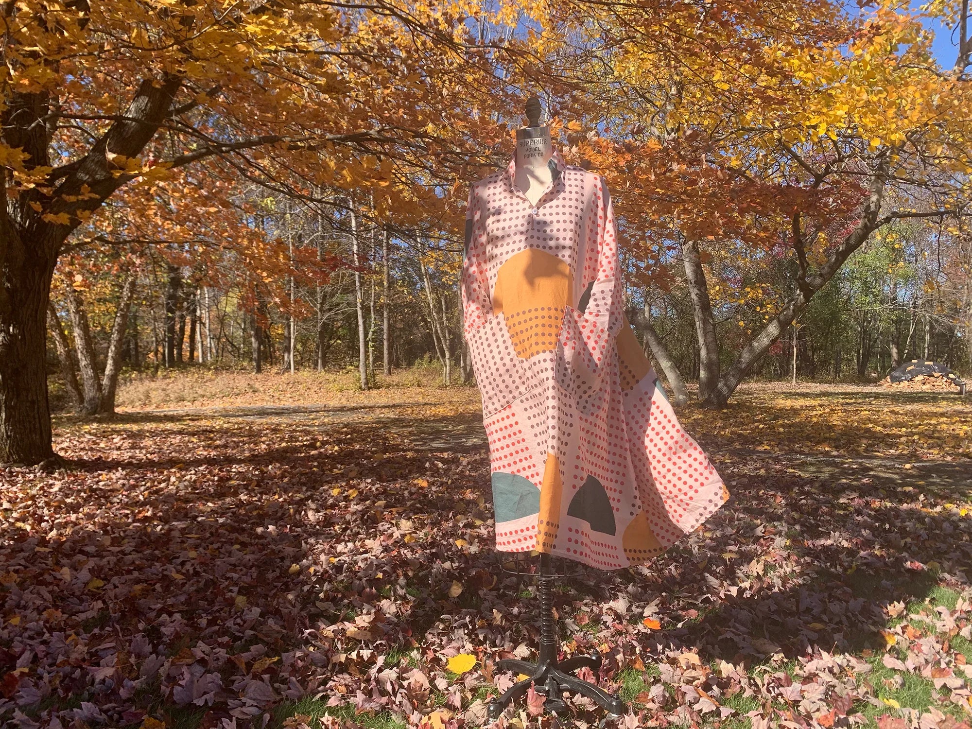 Colorful modern mu'umu'u dress with geometric Hawaiian print on mannequin outdoors in fall.