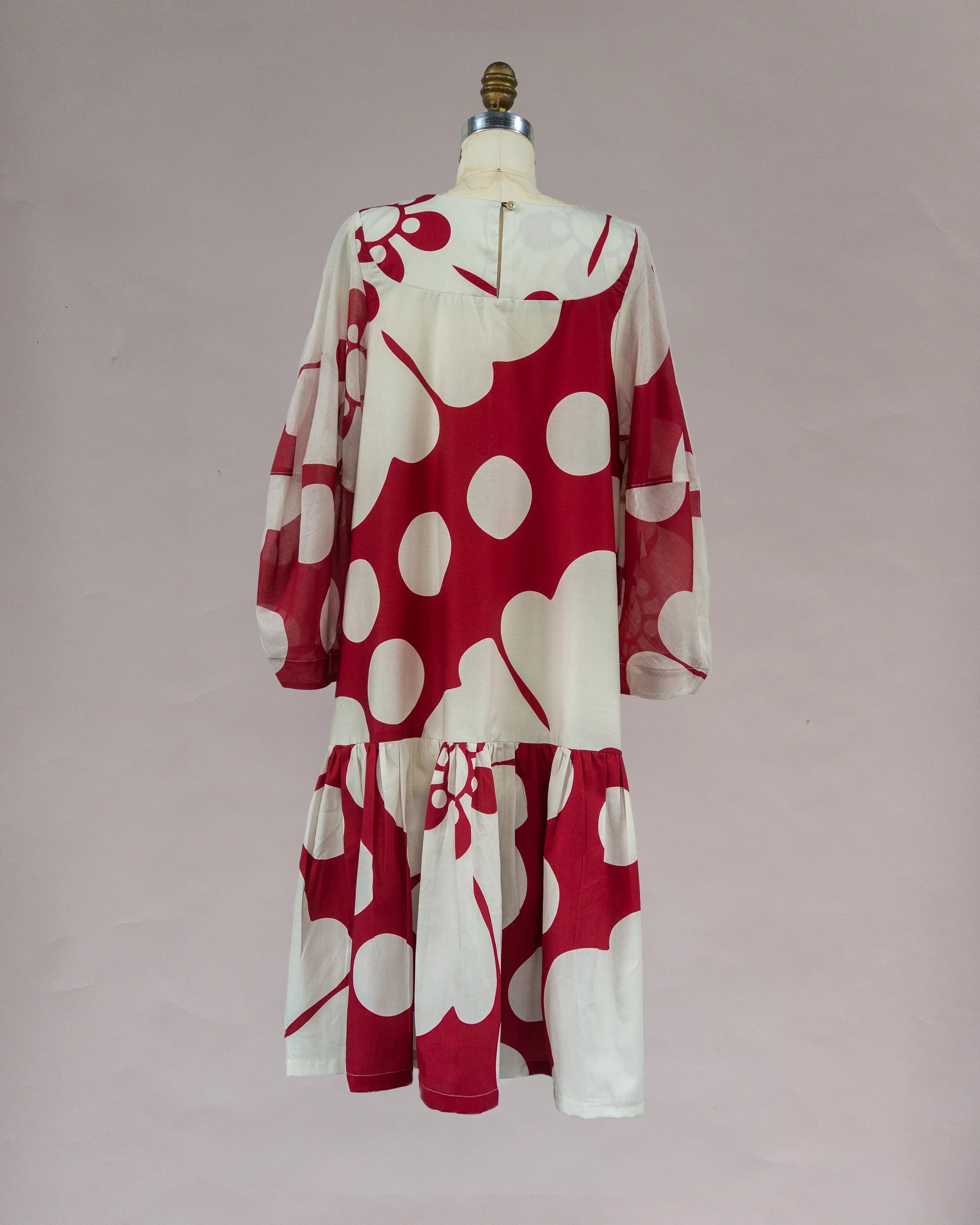 Red and white muumuu dress with bold floral print and long sleeves on mannequin