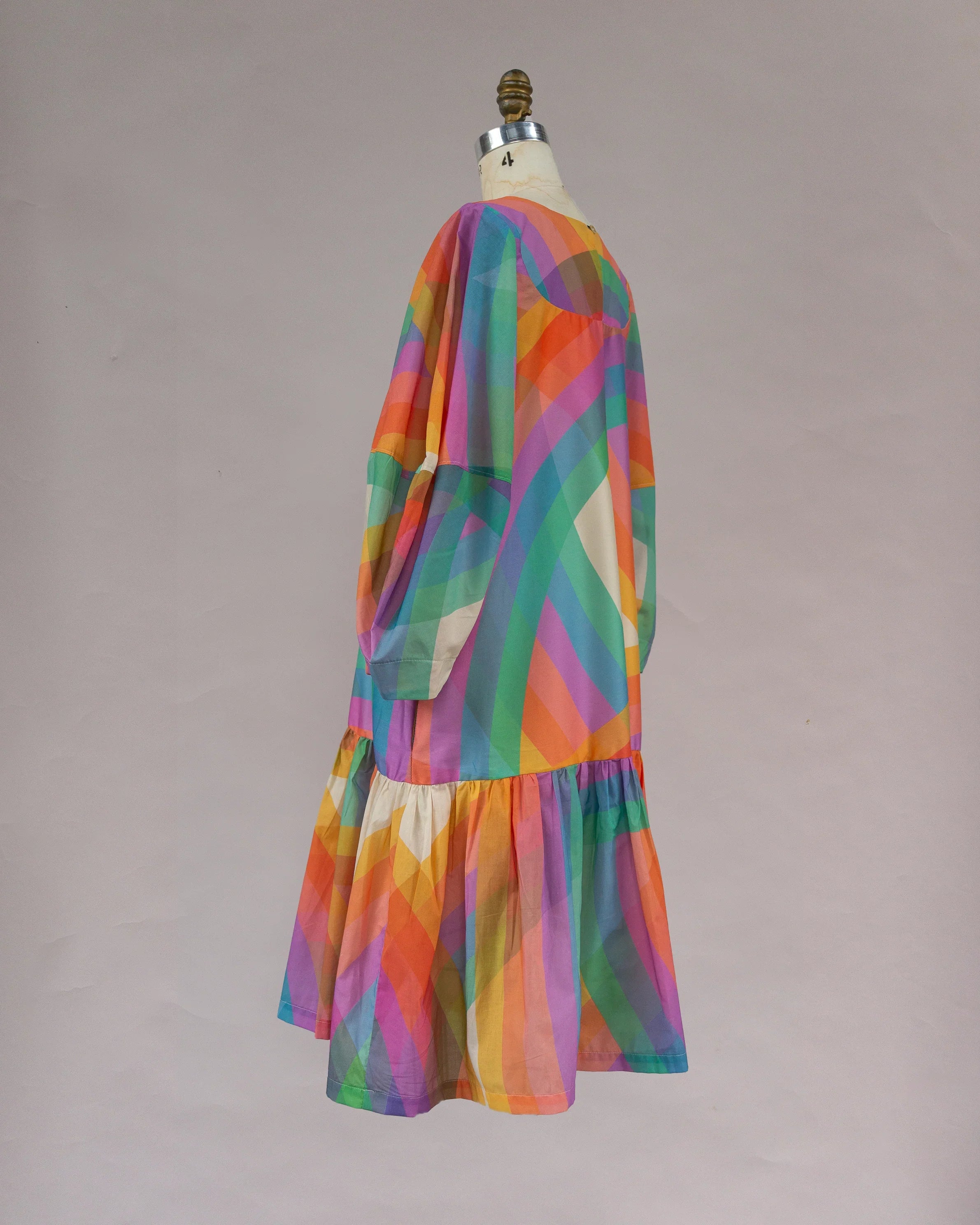 Colorful rainbow muʻumuʻu dress with geometric stripes and long sleeves on mannequin
