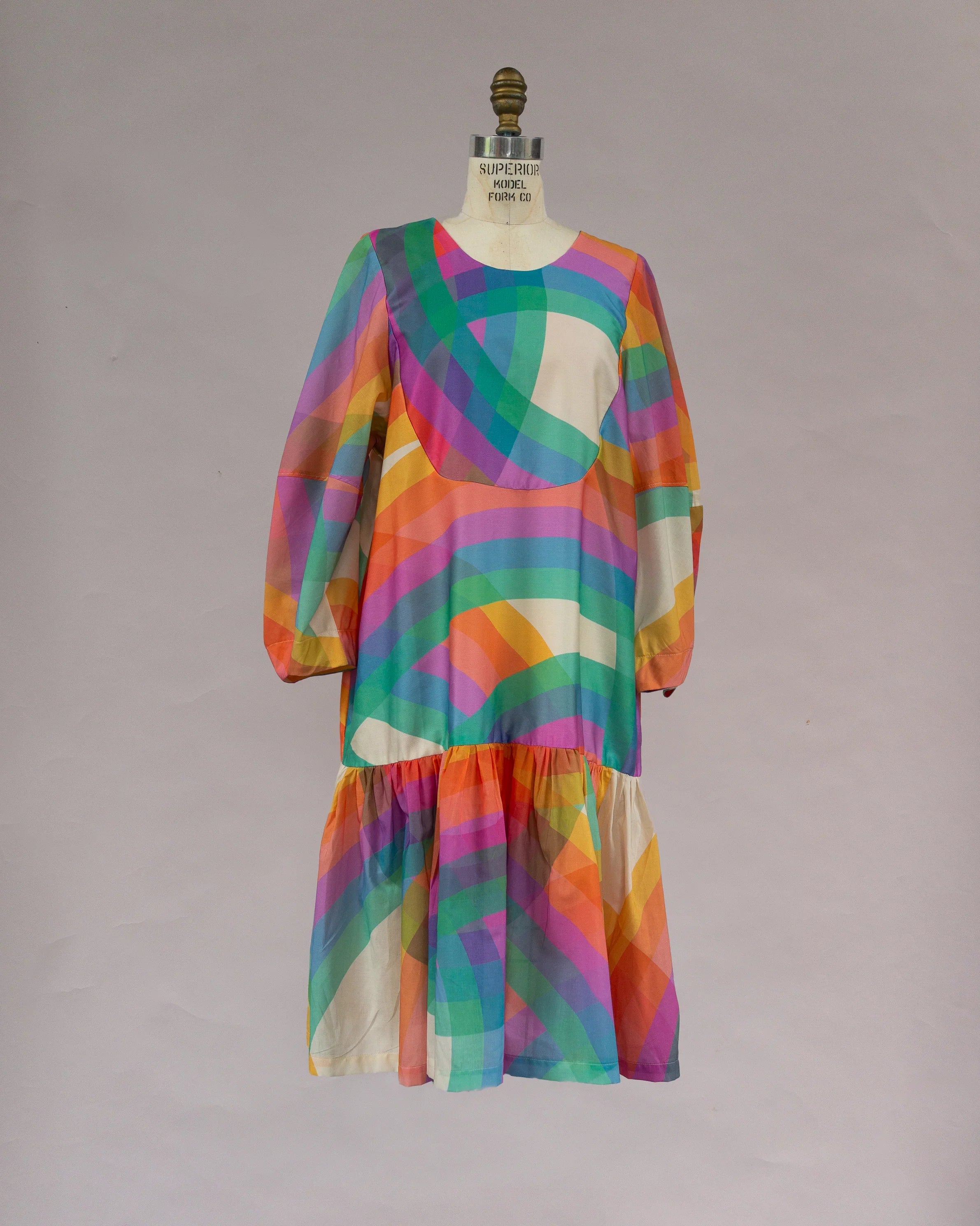 Modern mu'umu'u dress with long sleeves and vibrant rainbow geometric print on mannequin