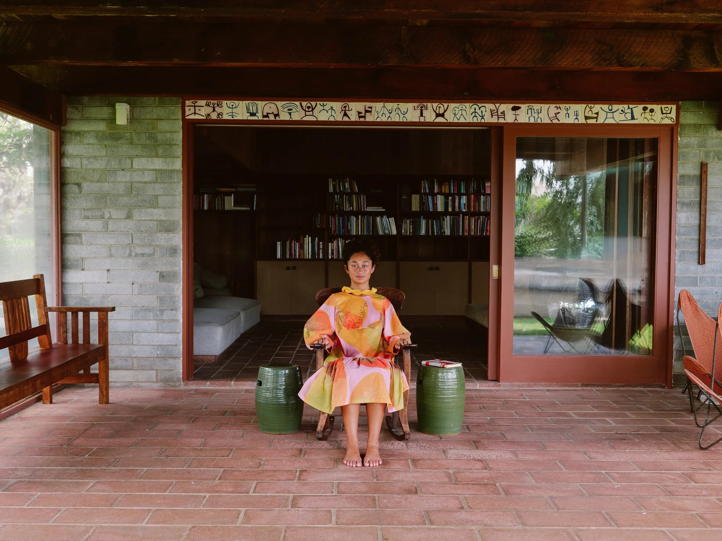 Woman in modern mu'umu'u dress with Hawaiian print seated on porch with brick and wood decor