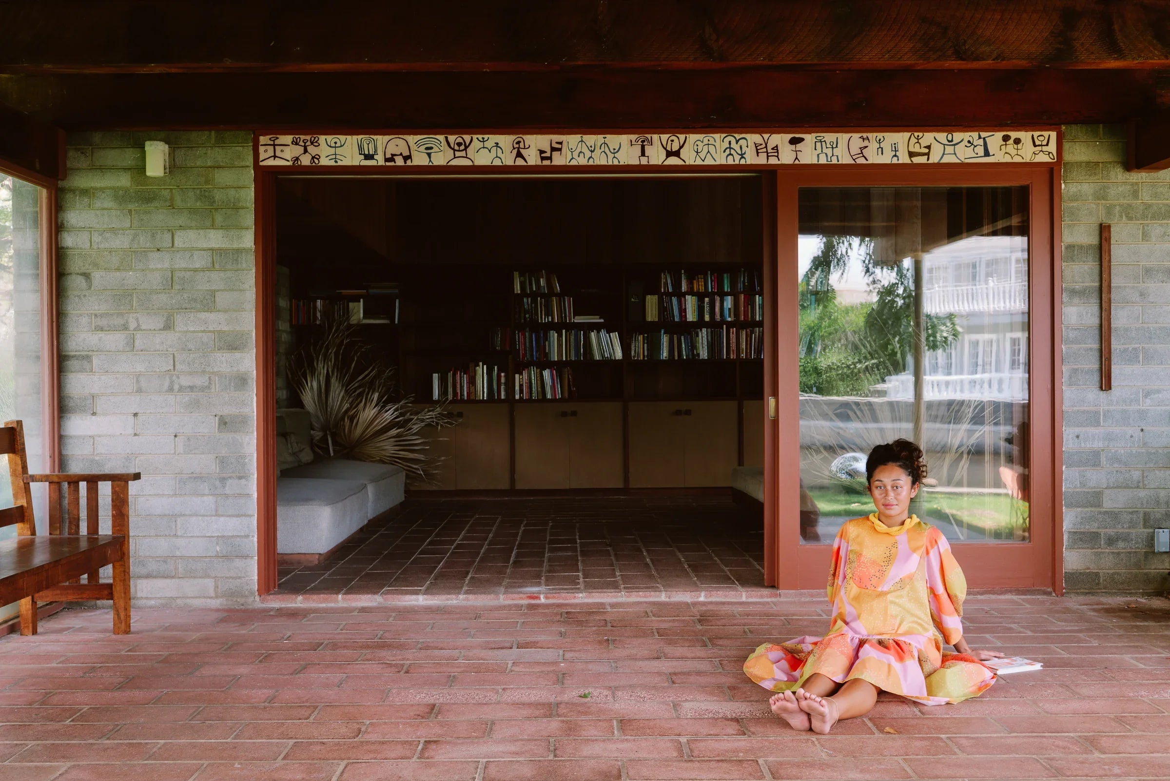 Woman in a colorful modern mu'umu'u dress sitting on a brick patio, library in background
