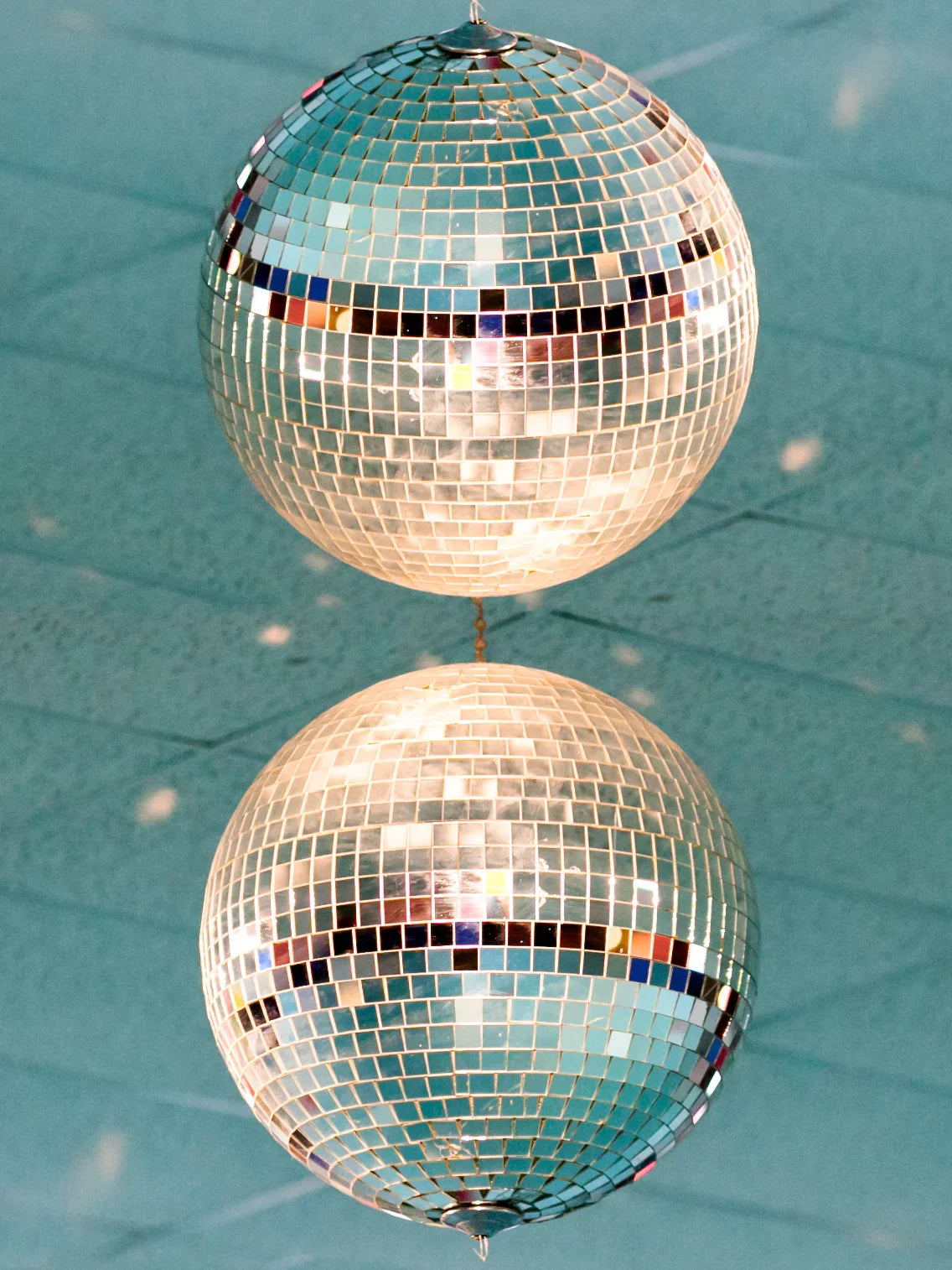 Two mirrored disco balls reflecting light on a blue ceiling background