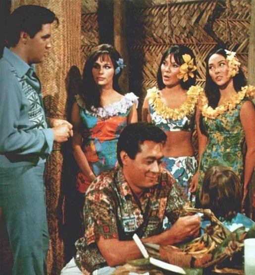 Group of people in colorful Hawaiian print mu'umu'u dresses with tropical decor