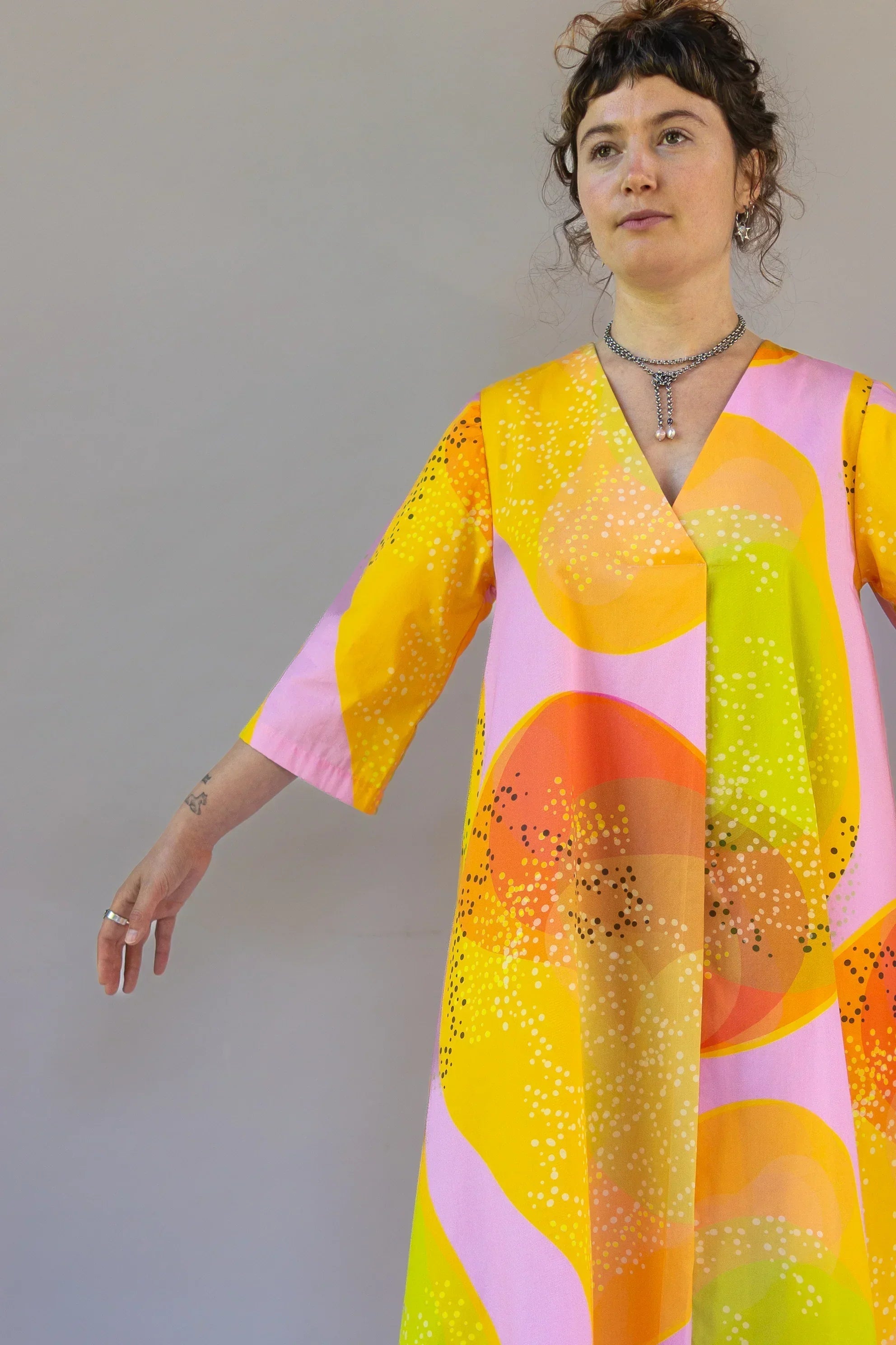 Woman wearing a modern mu'umu'u dress with yellow, orange, and pink Hawaiian print