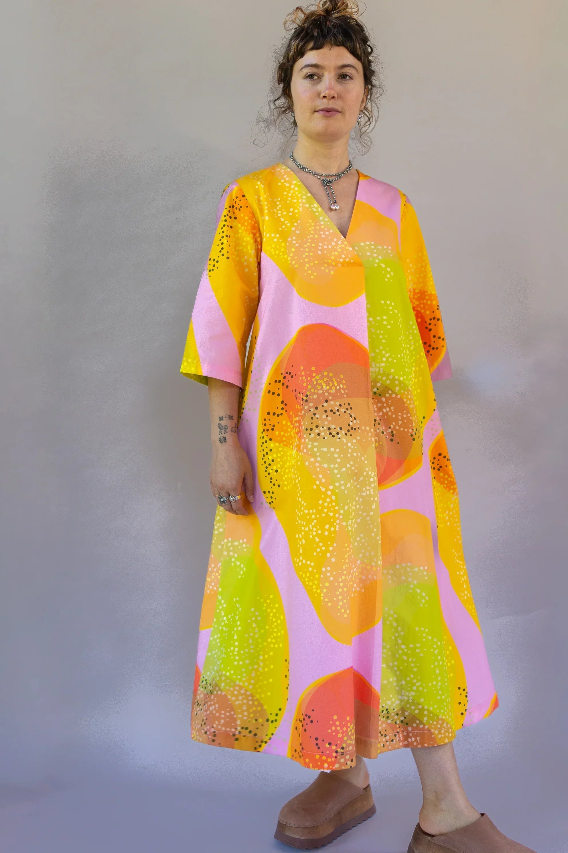 Woman wearing modern muumuu dress with pink, yellow, and orange Hawaiian-inspired print