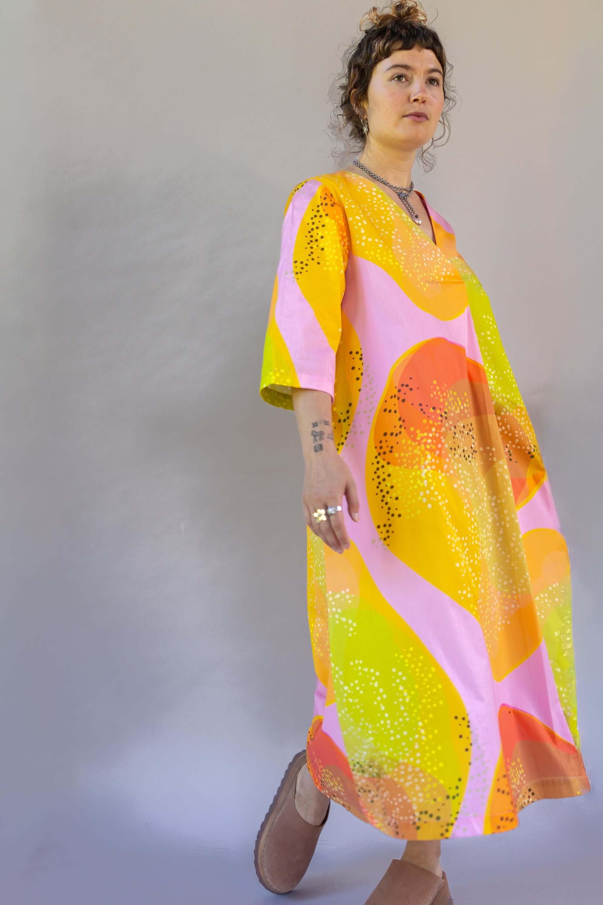 Woman wearing a colorful modern mu'umu'u dress with abstract yellow, pink, and orange print