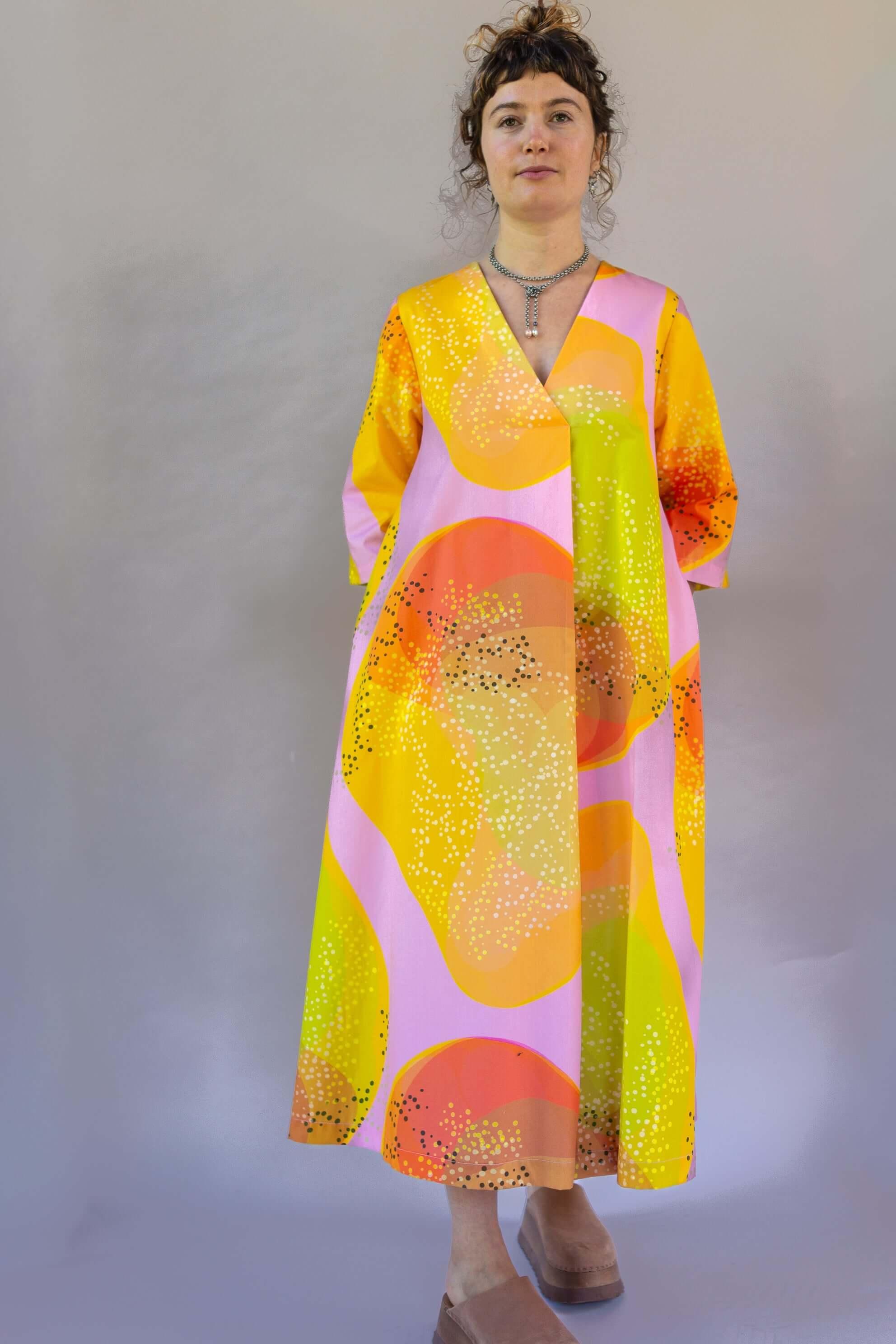 Woman wearing modern muumuu dress with bold orange, yellow, and pink Hawaiian print
