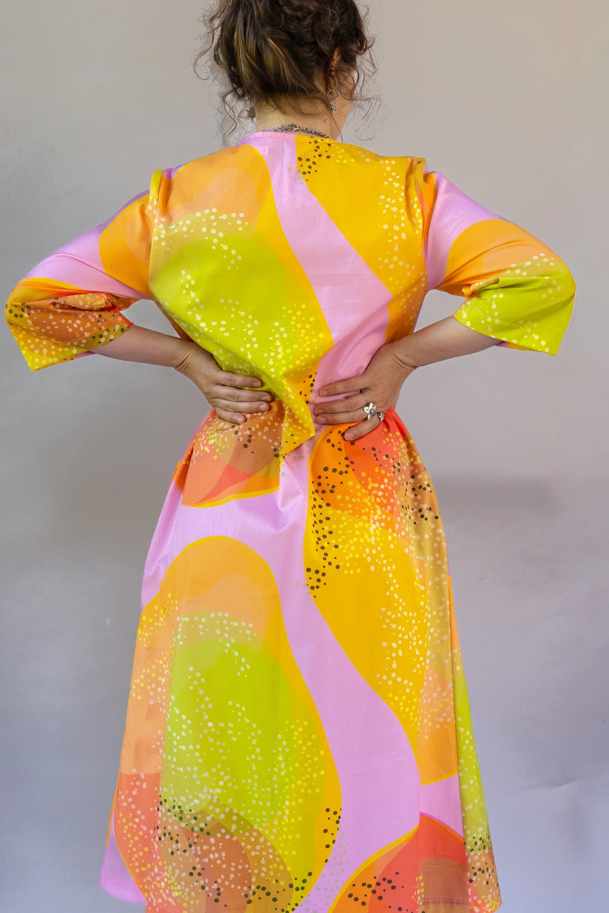 Woman wearing modern muumuu dress with vibrant yellow, pink, and orange abstract print