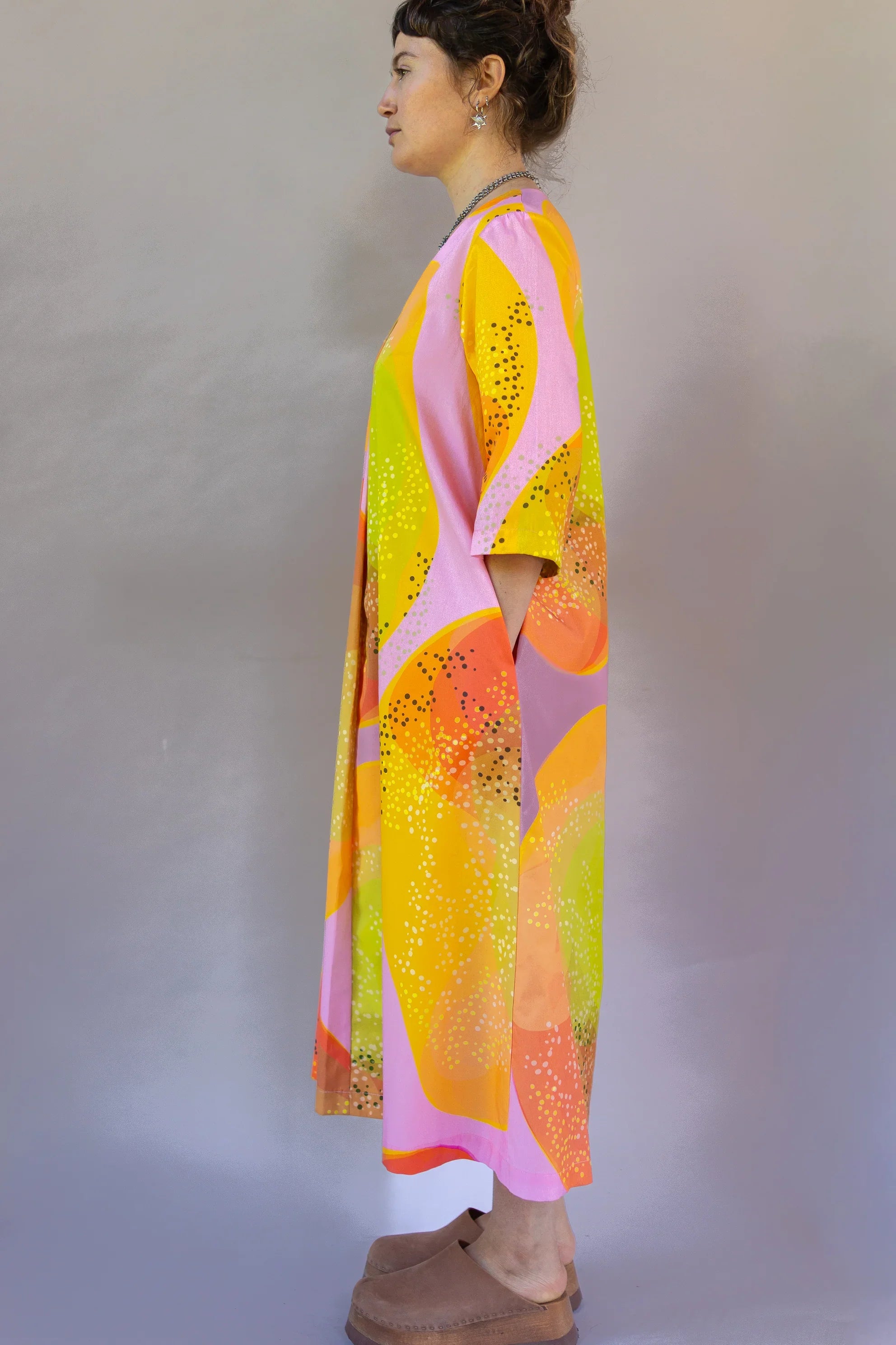 Woman in side profile wearing a vibrant modern muumuu dress with pink, yellow, and orange abstract Hawaiian print