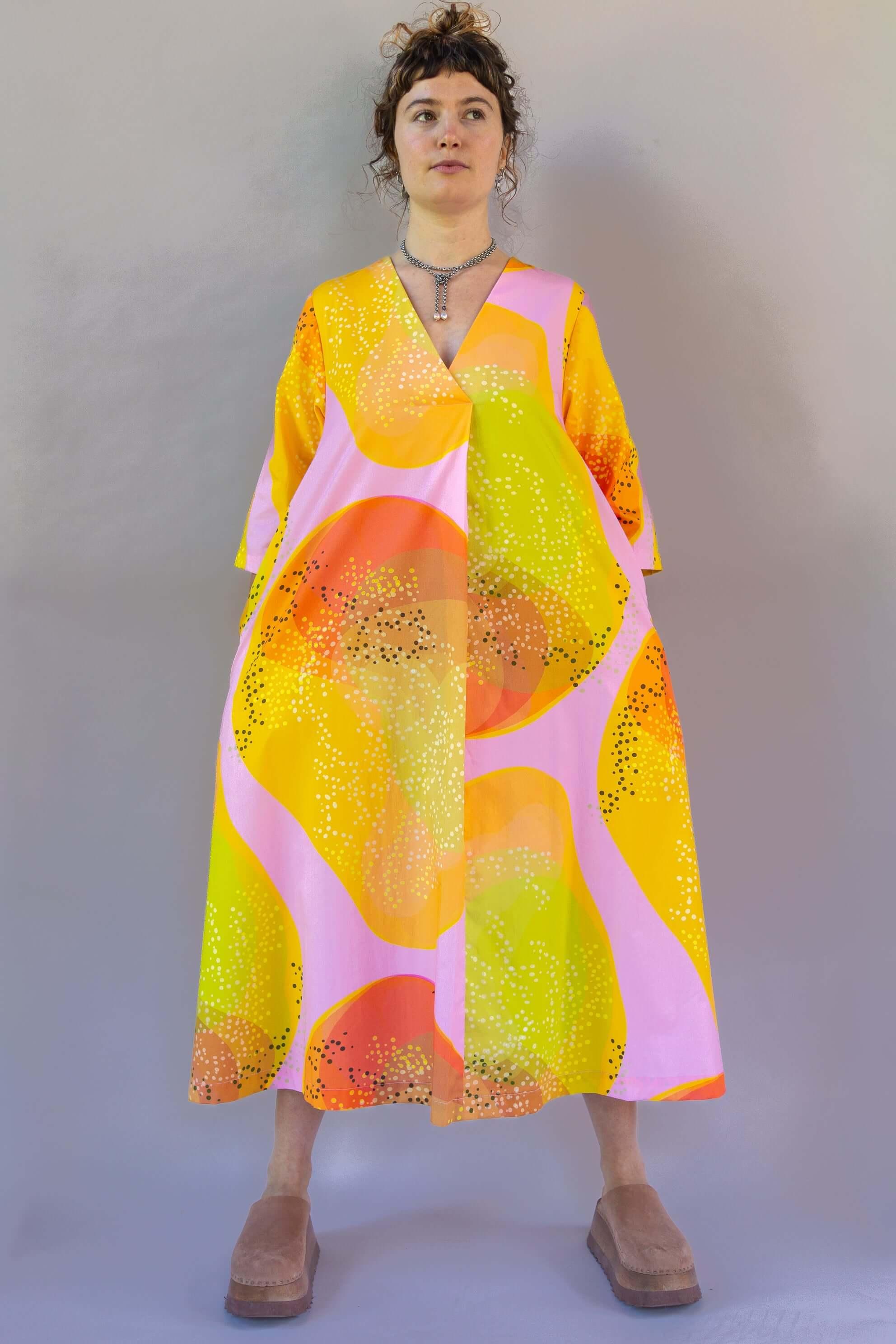 Woman wearing a modern muumuu dress with bright yellow, orange, and pink abstract print