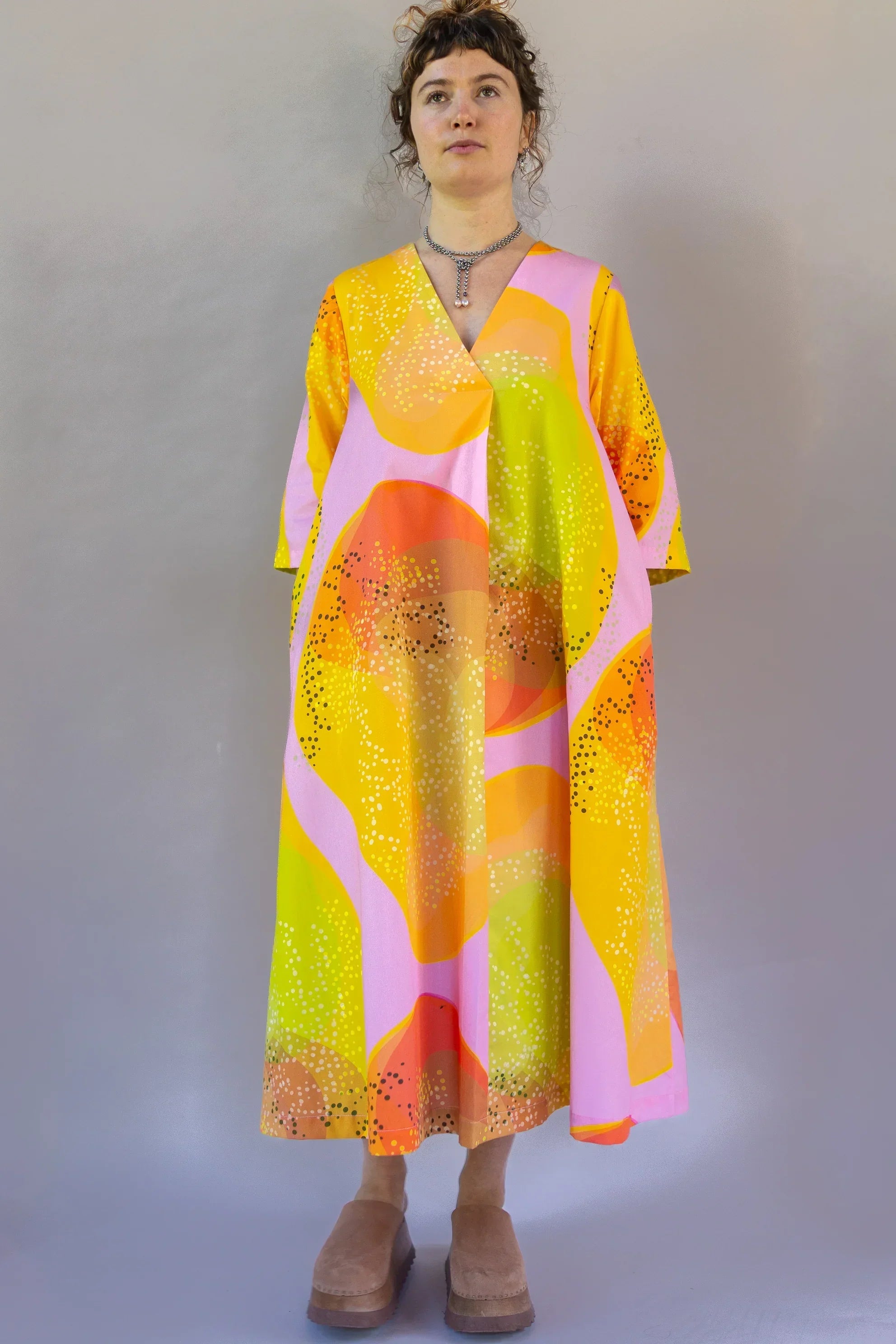 Woman wearing a modern muumuu dress with bold pink, orange, and yellow Hawaiian print