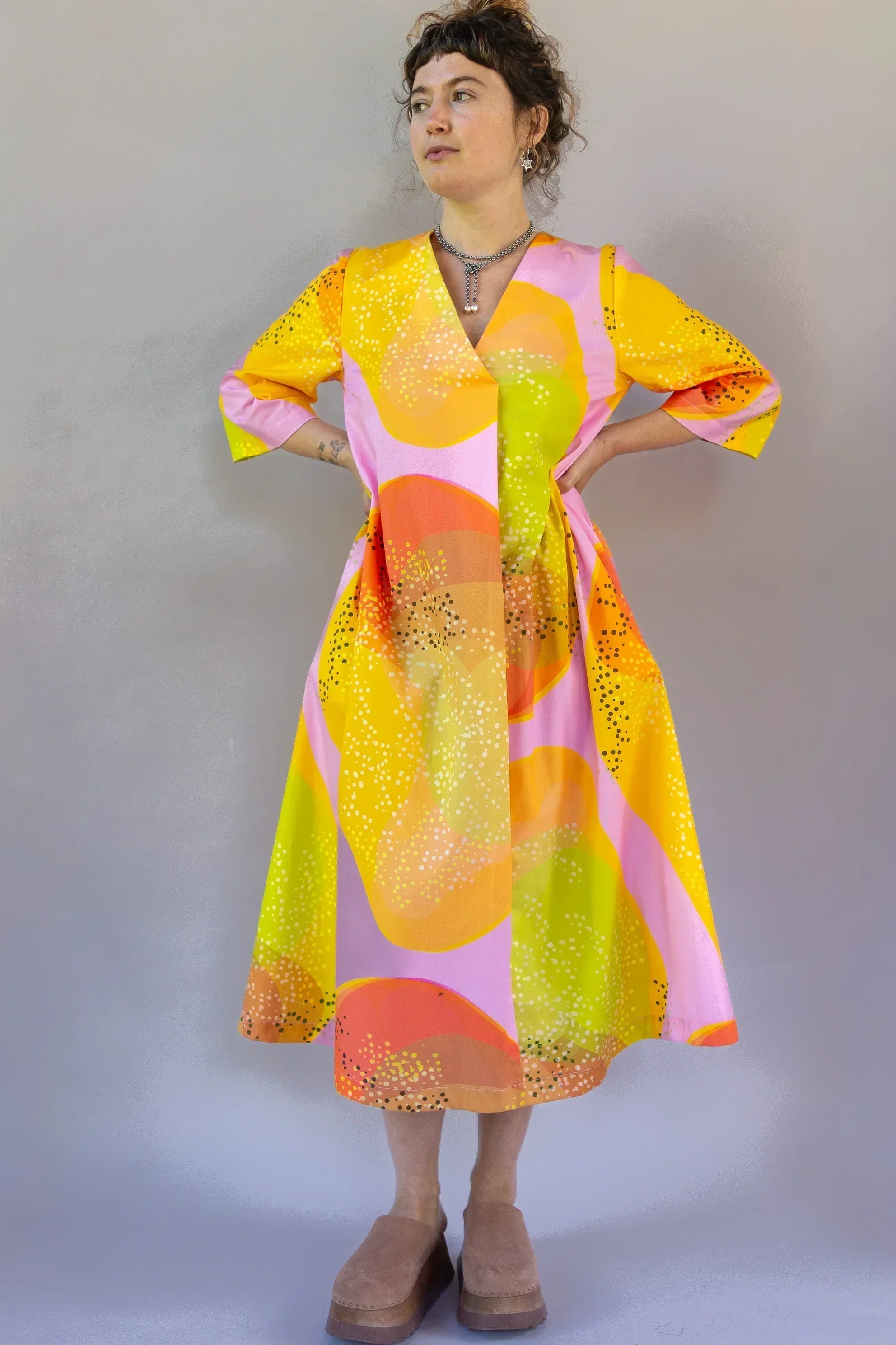 Woman wearing a modern muumuu dress with vibrant orange, yellow, and pink Hawaiian print