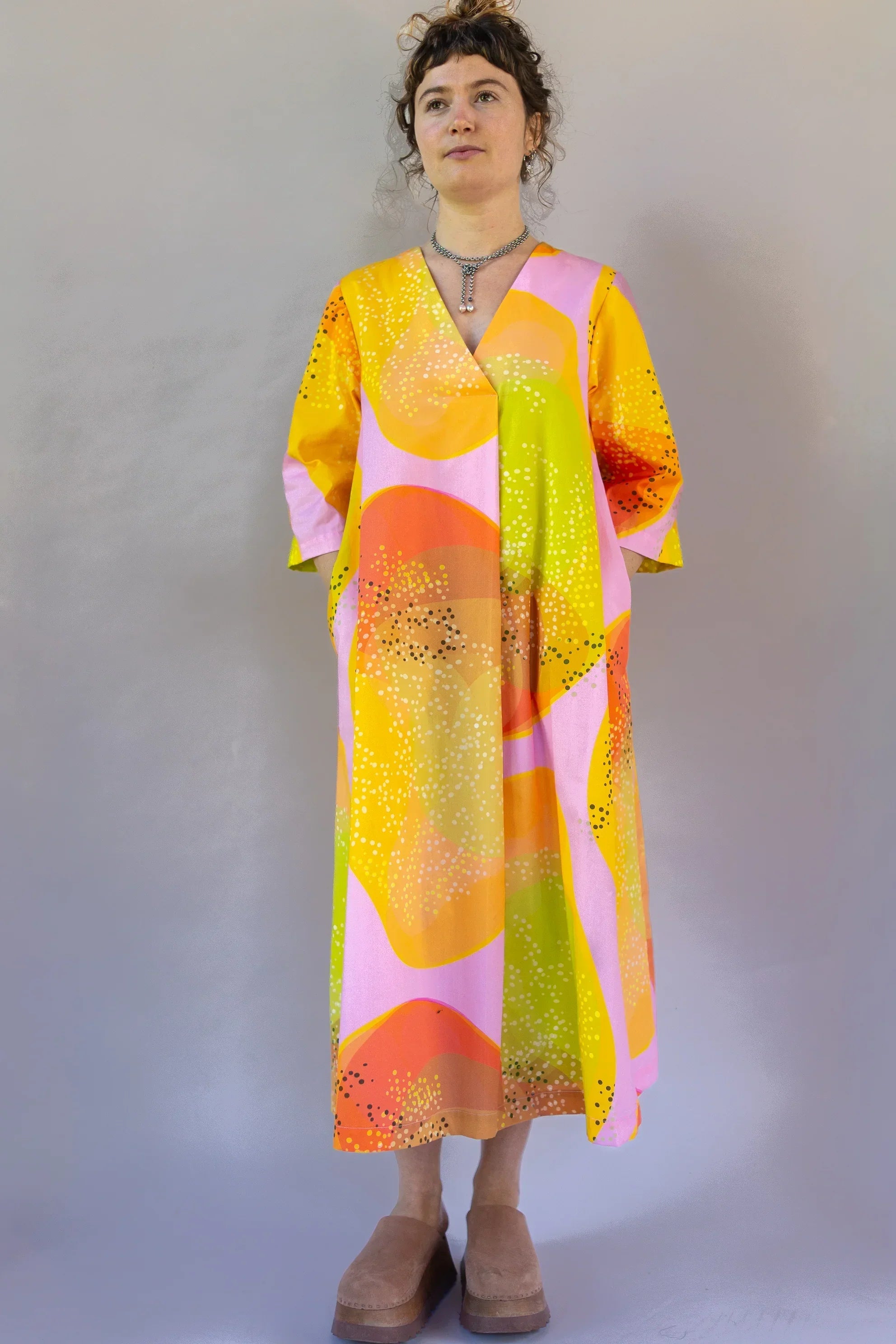 Woman wearing a modern mu'umu'u dress with vibrant yellow, pink, and orange Hawaiian print