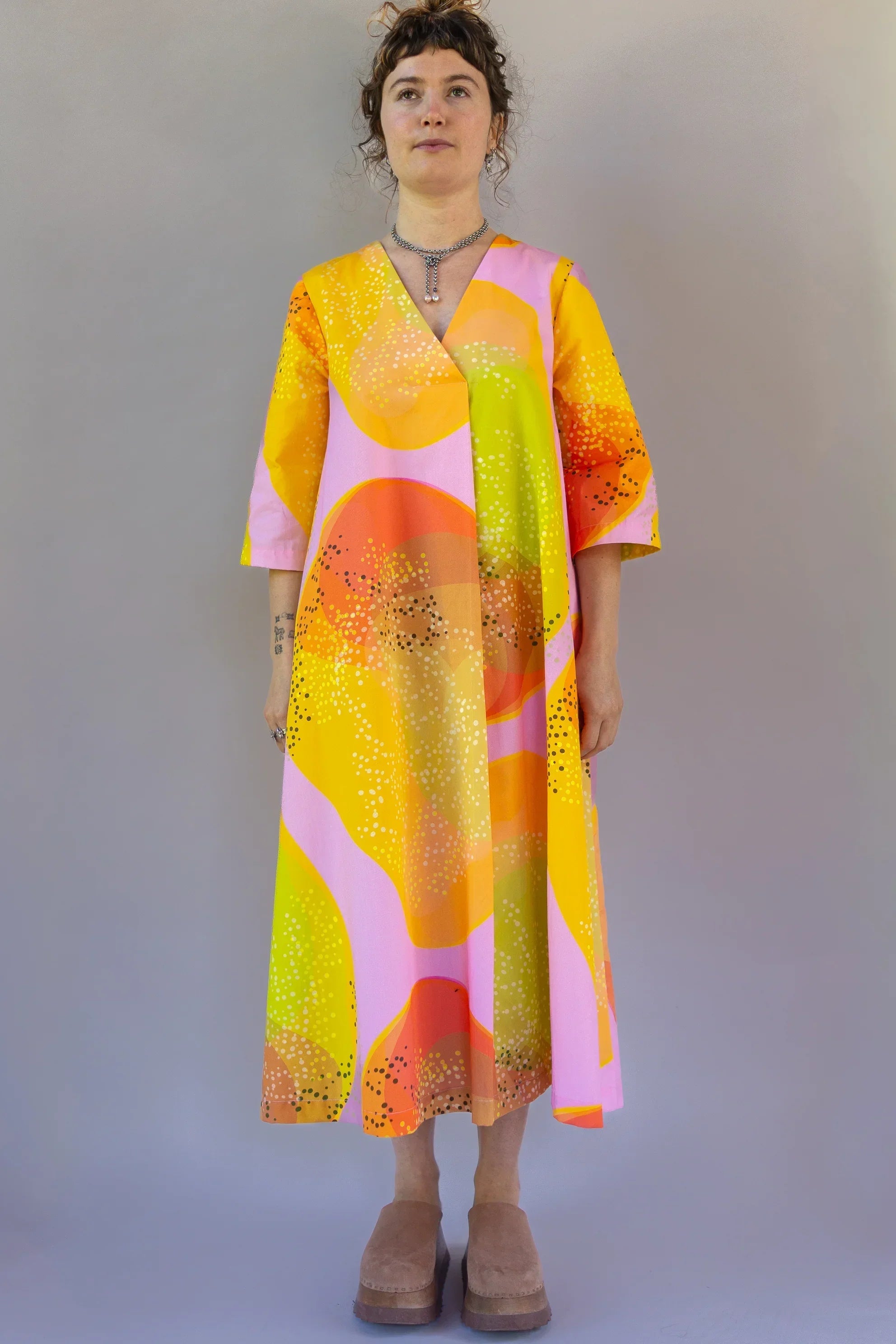 Woman wearing modern muumuu dress with colorful yellow, orange, and pink Hawaiian print