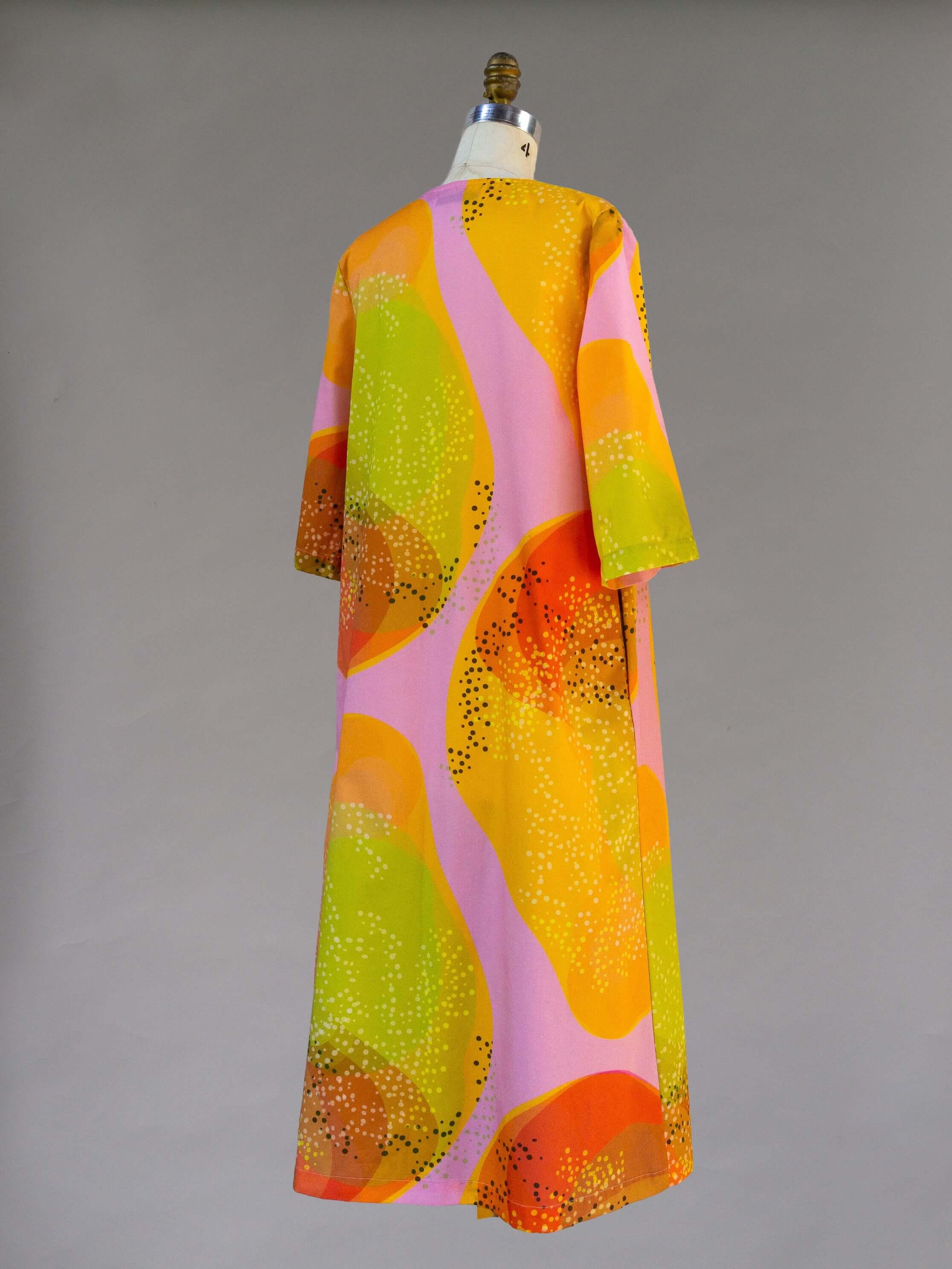 Modern muumuu dress with vibrant mango, orange, pink, and green Hawaiian print, back view