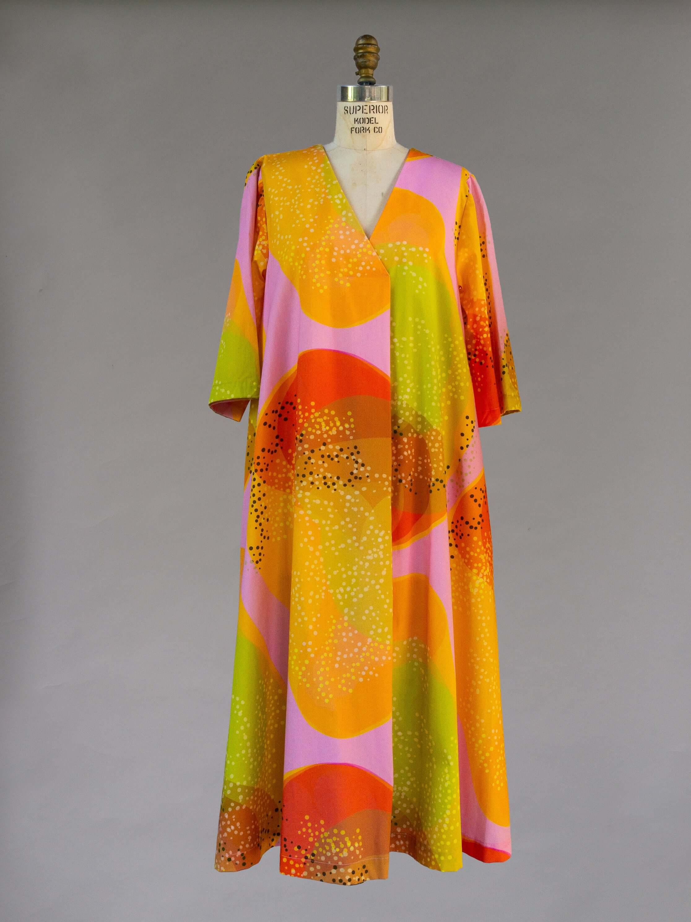 Colorful modern mu'umu'u dress with abstract orange, yellow, and pink Hawaiian print on a mannequin