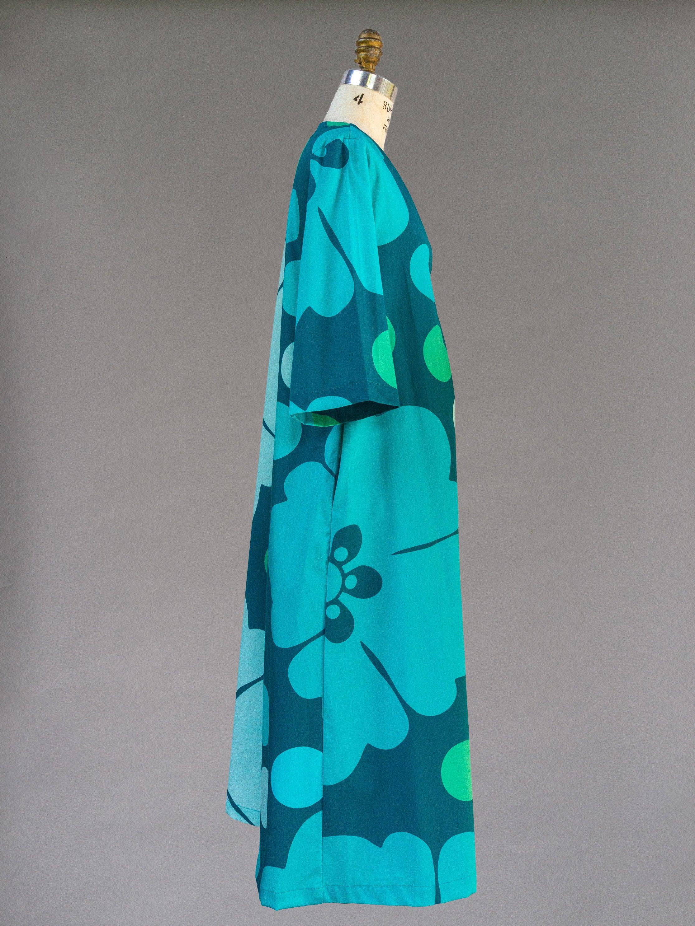 Teal pareo dress with bold Hawaiian floral print, draped on a mannequin, side view