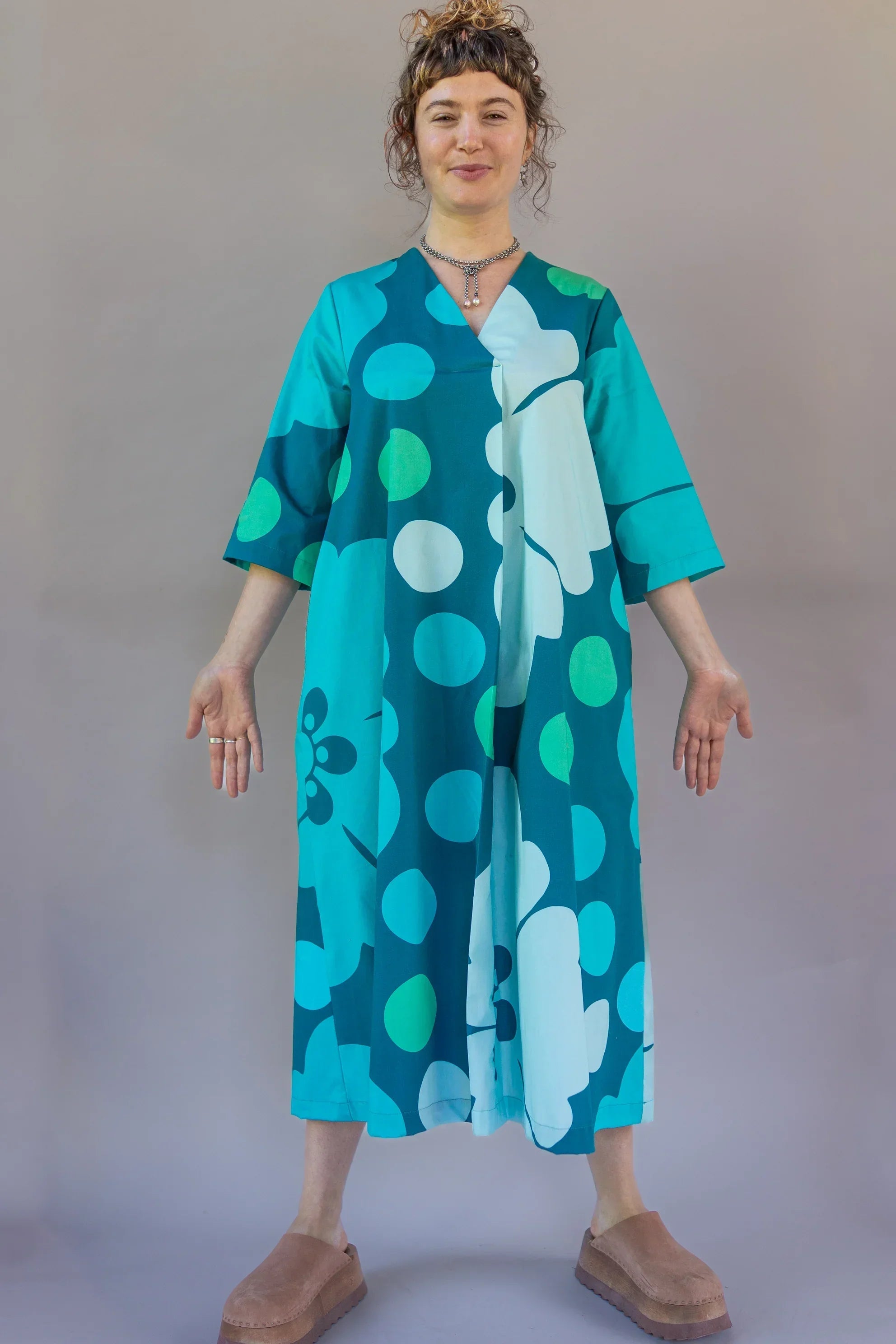 Woman wearing a blue Hawaiian print modern muumuu dress with bold teal polka dots