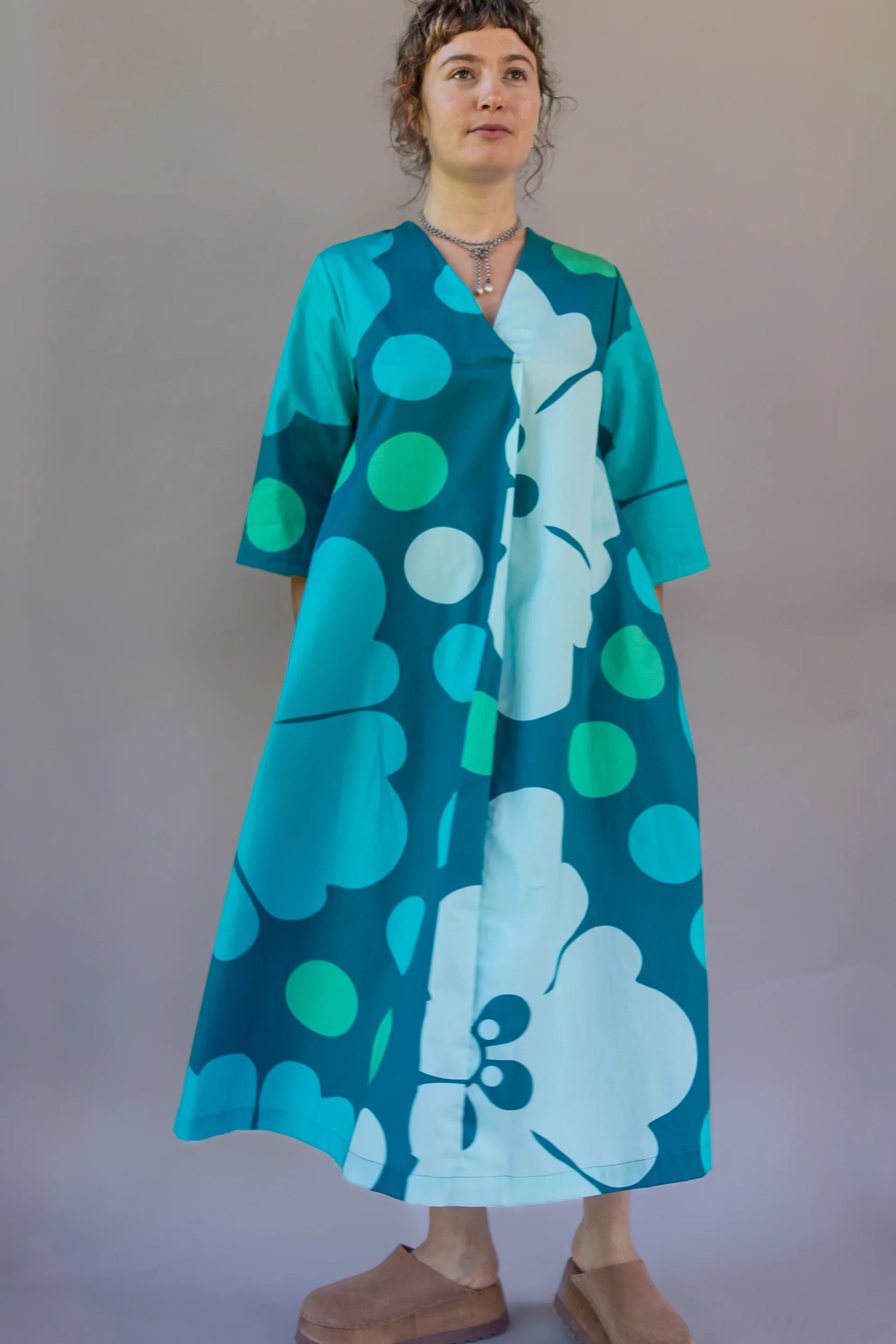 Woman wearing a teal Hawaiian print mu'umu'u dress with floral and polka dot design