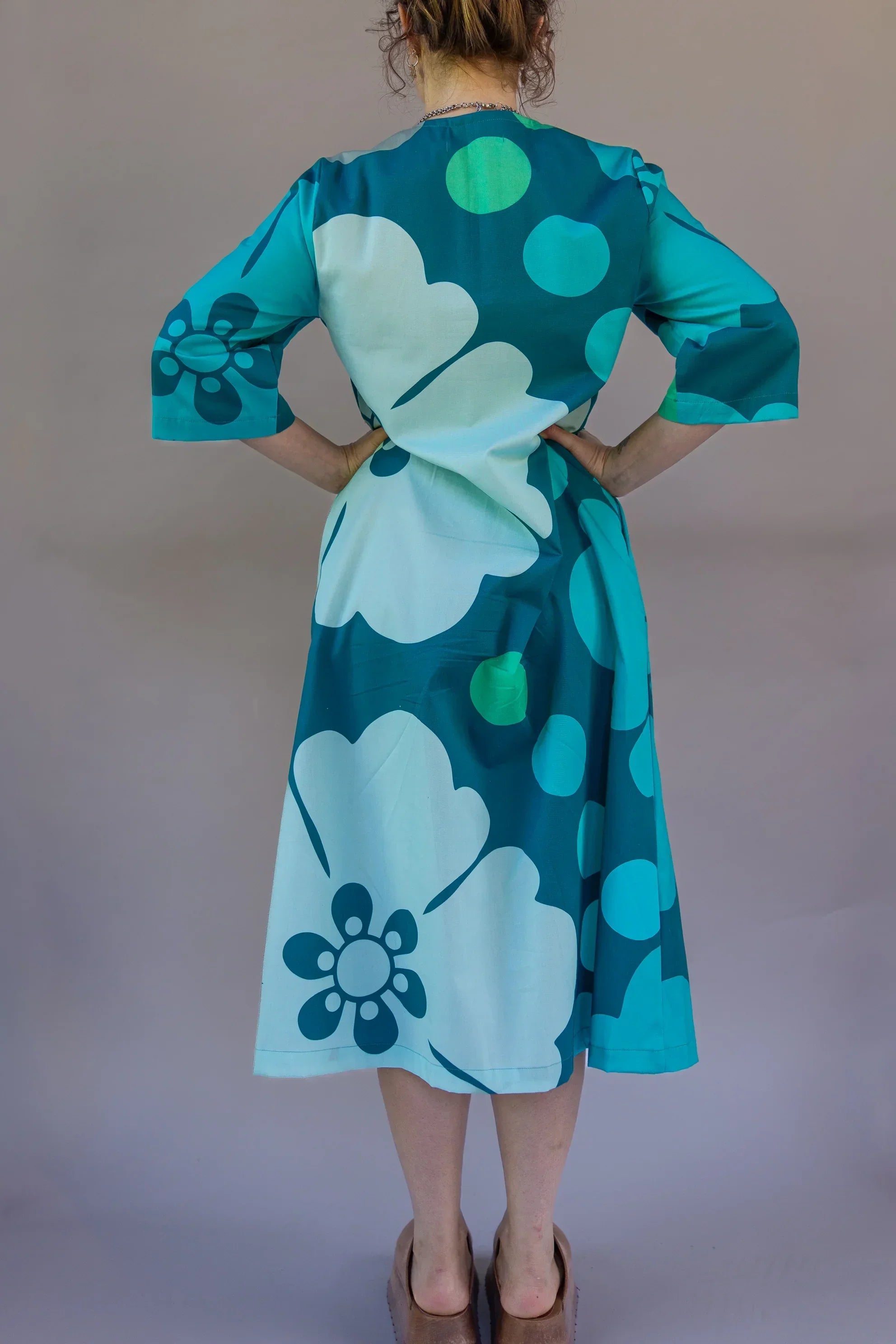 Back view of a woman wearing an ocean blue floral Hawaiian pareo dress with 3/4 sleeves