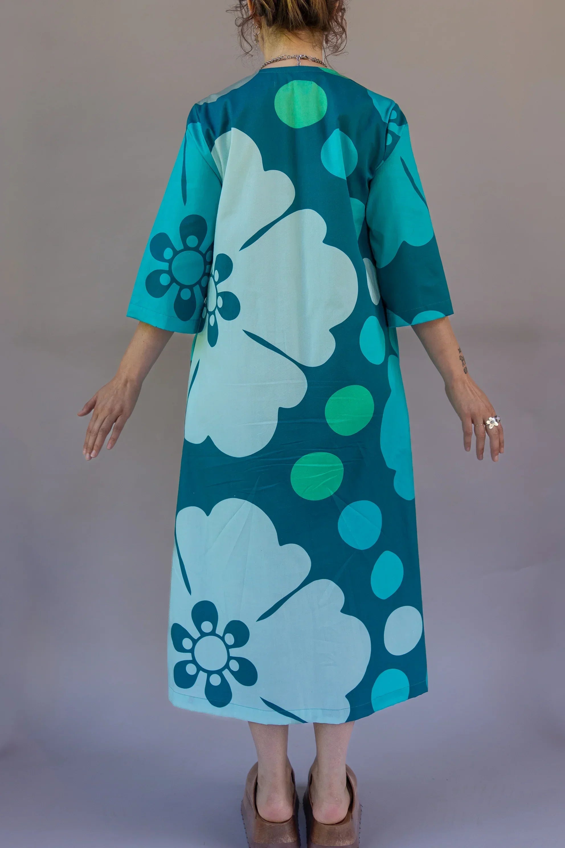 Back view of a woman wearing a teal Hawaiian muumuu dress with bold floral print
