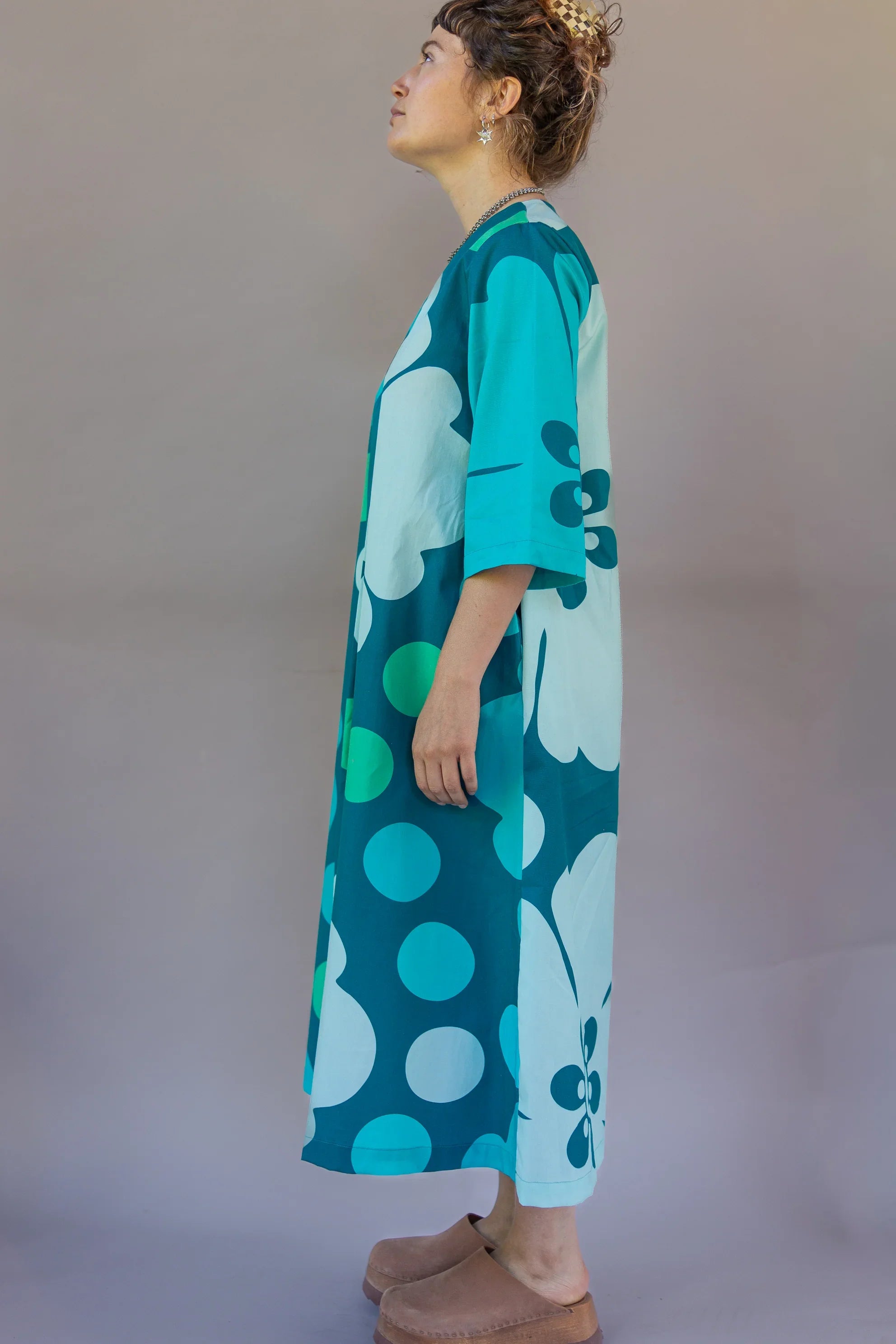 Woman in a teal, blue, and green floral Hawaiian muumuu dress with bold prints, side view
