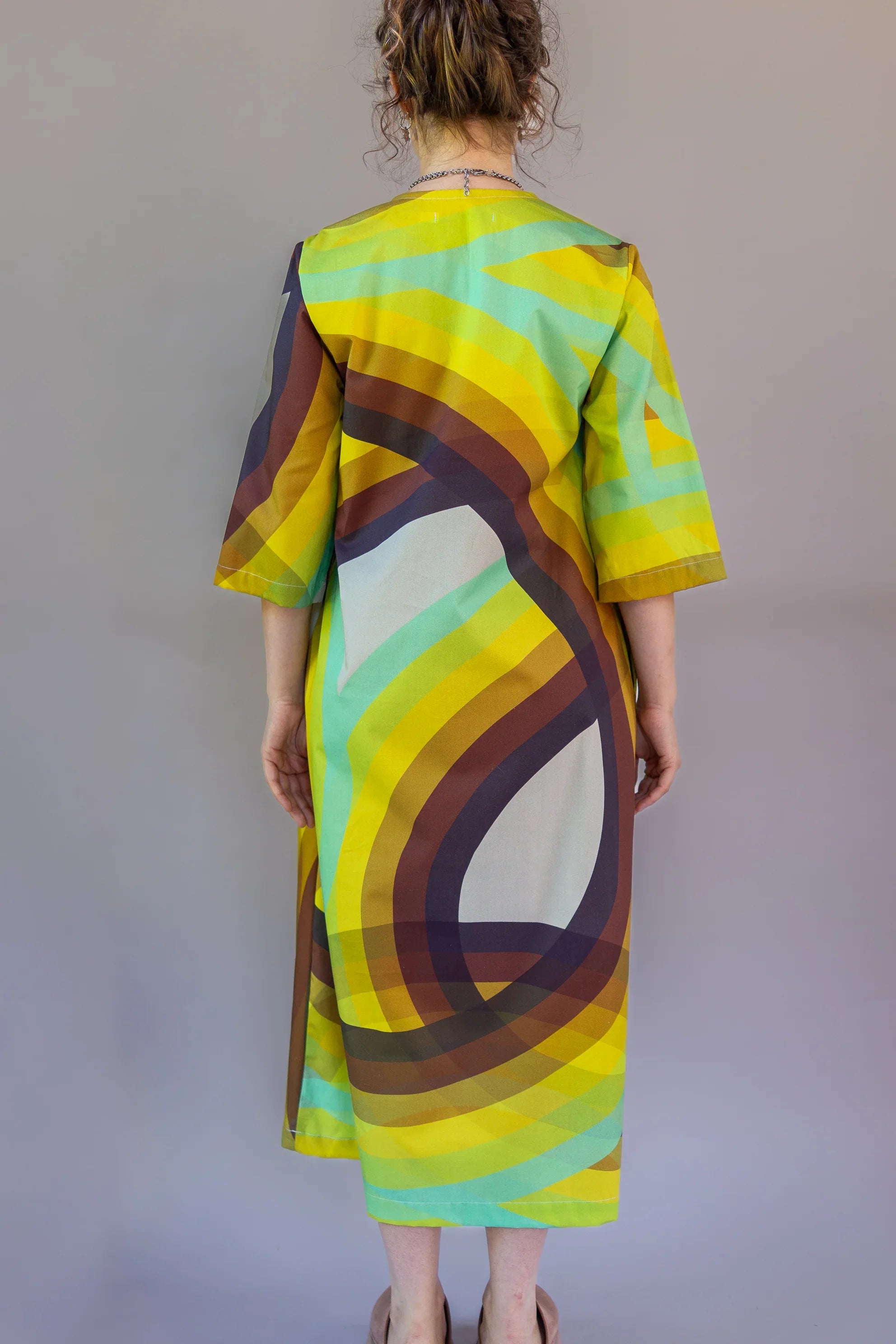 Woman wearing modern muumuu dress with colorful abstract rainbow pattern, back view