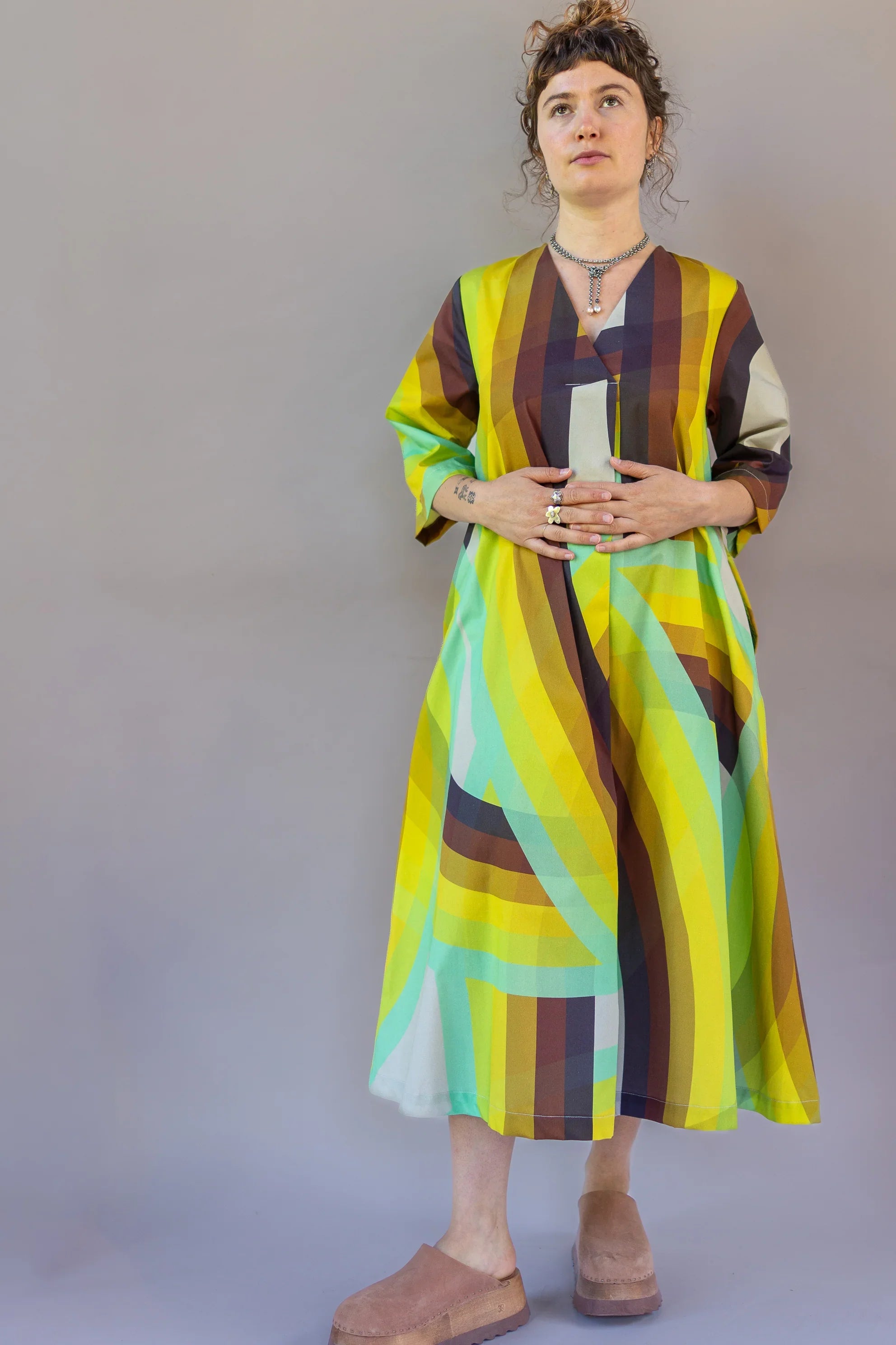 Woman wearing a modern muumuu dress with bold yellow, green, and brown geometric print