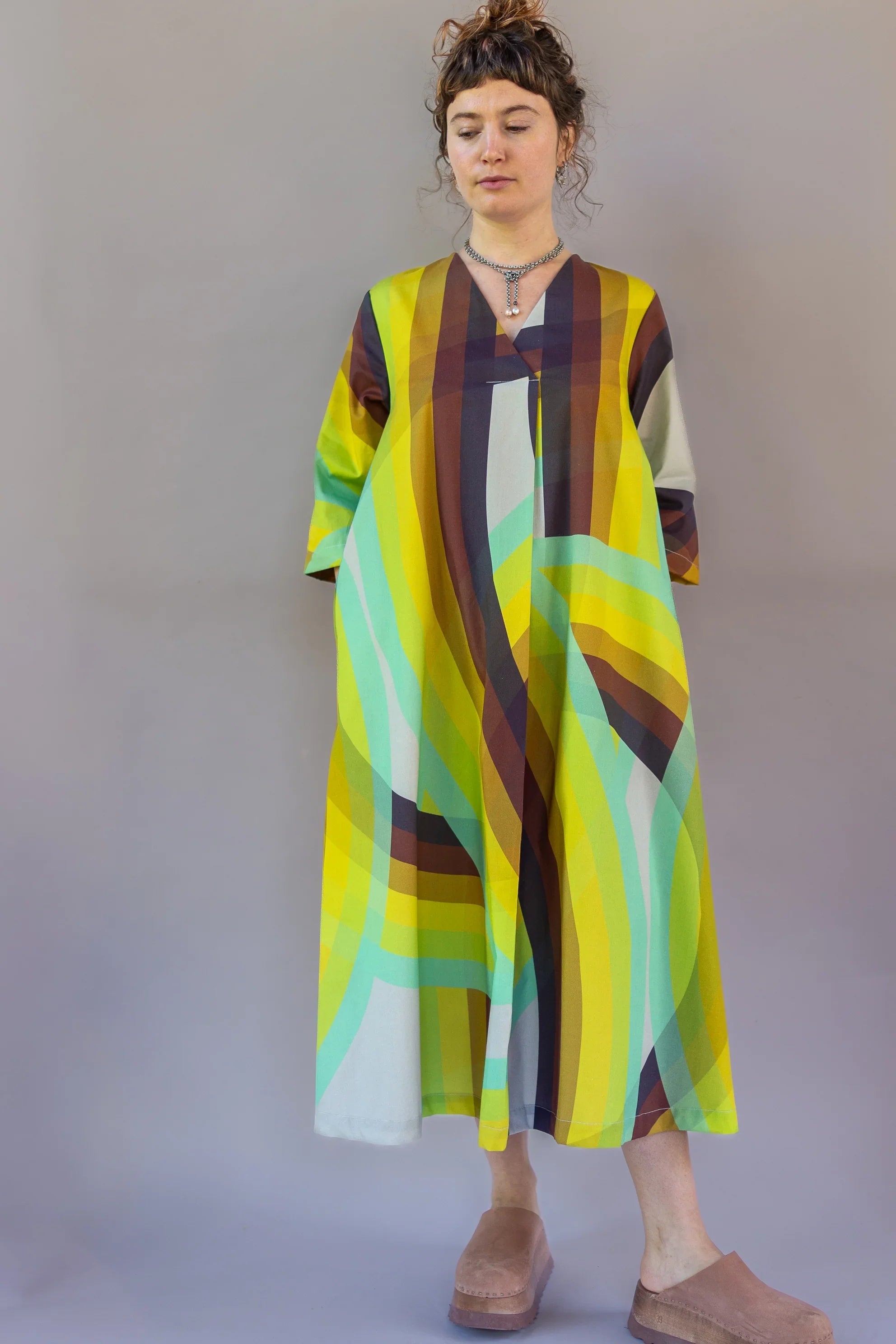 Woman wearing a modern muumuu dress with bold yellow, green, and brown abstract print