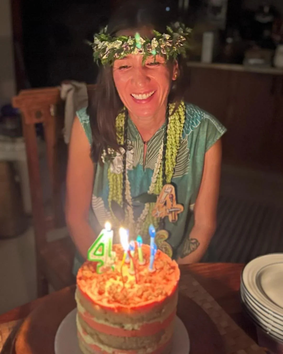 Woman in leafy Hawaiian dress and flower crown smiling at birthday cake with candles