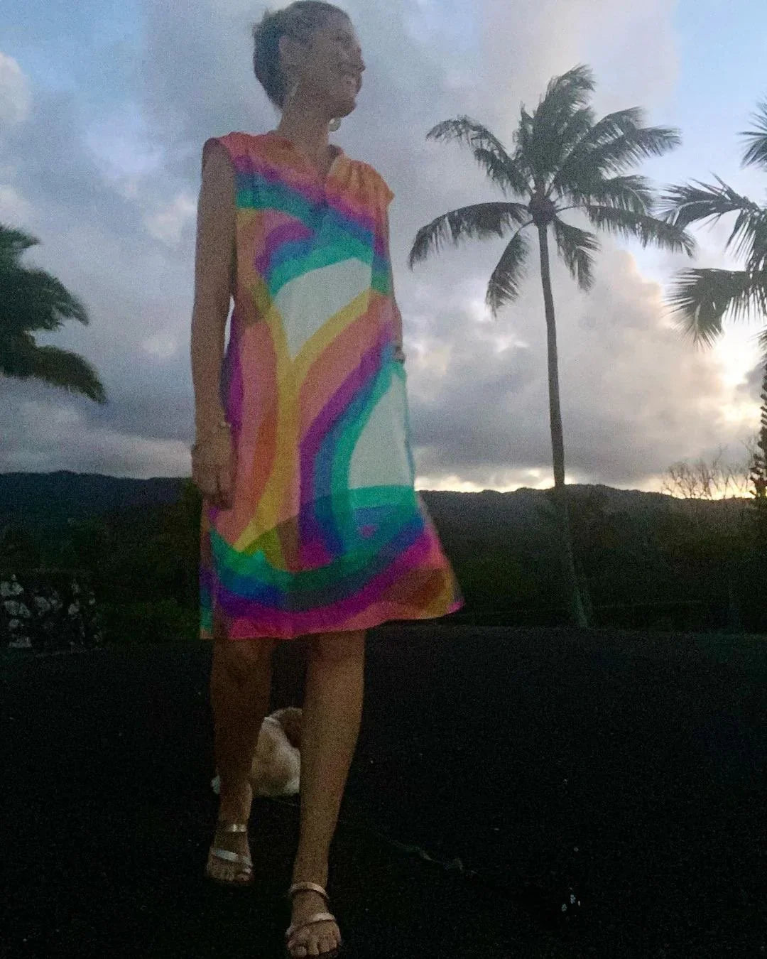 Woman in a colorful modern muumuu dress outdoors with palm trees at sunset