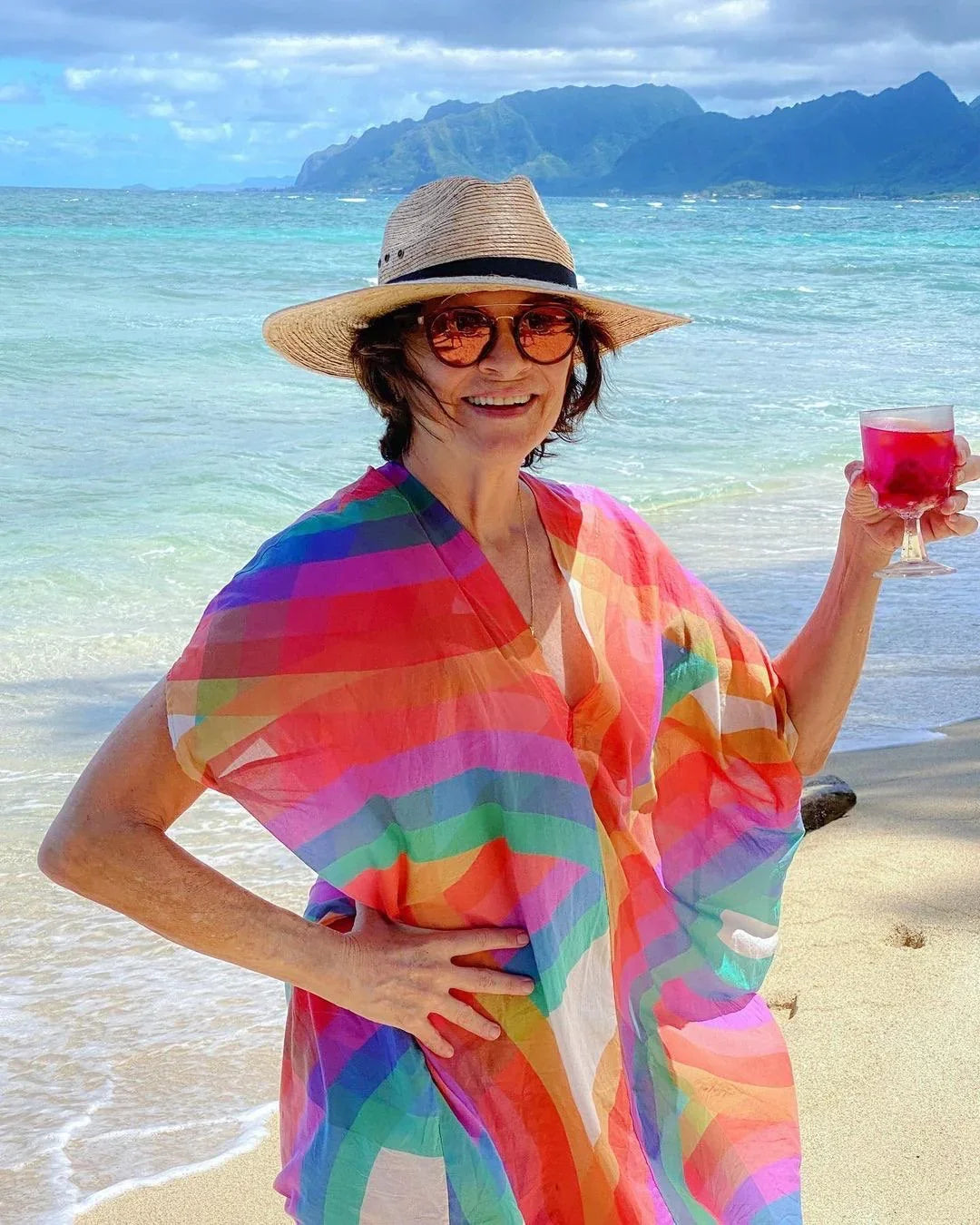 Woman in a colorful modern muumuu dress, wearing a sun hat and sunglasses on a Hawaiian beach