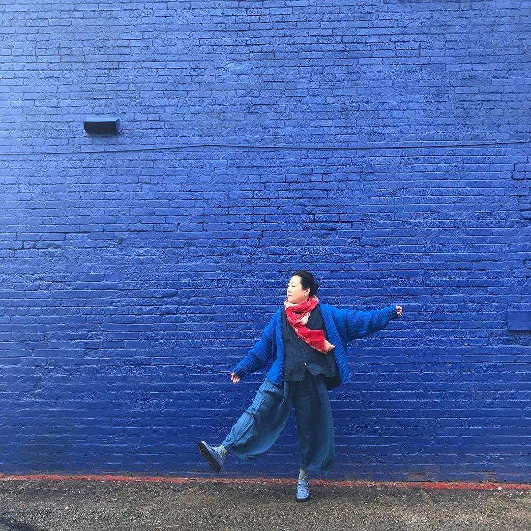 Woman in loose blue outfit and red scarf posing by vibrant blue brick wall