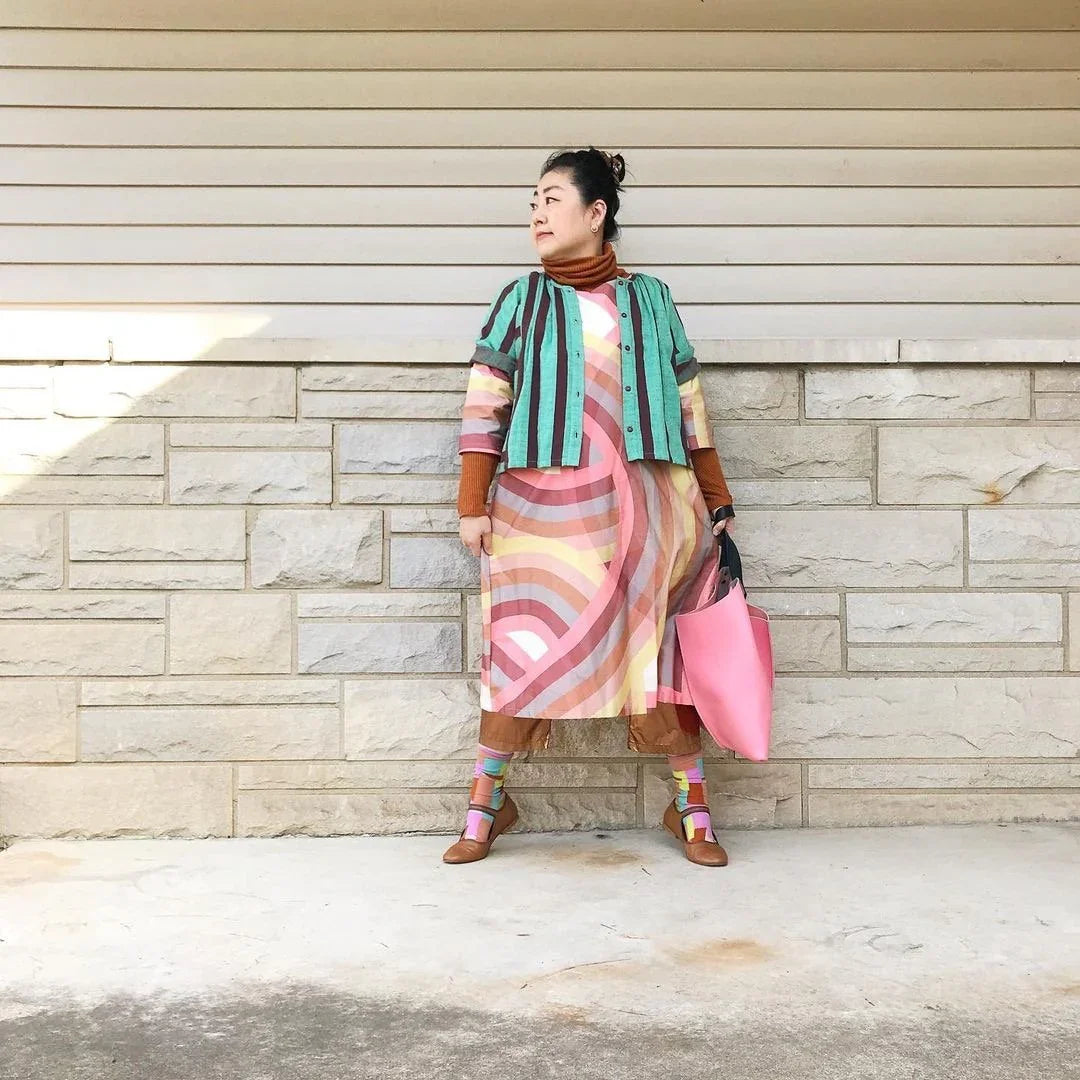 Woman in colorful modern mu'umu'u dress with geometric pattern, holding pink tote bag