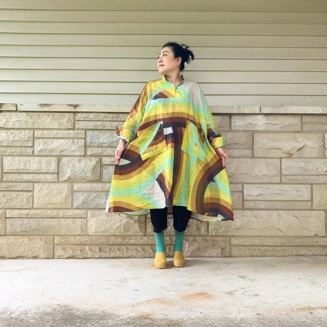 Woman wearing a modern mu'umu'u dress with colorful Hawaiian print standing by stone wall
