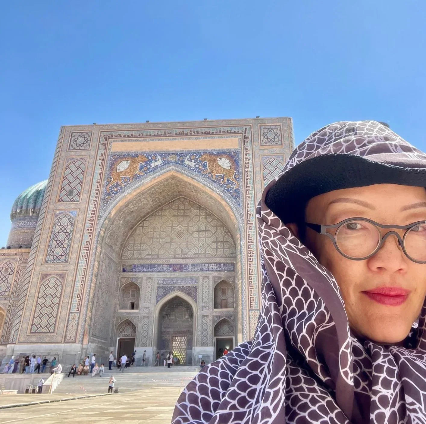 Woman in printed scarf and glasses in front of ornate, mosaic-tiled Islamic architecture