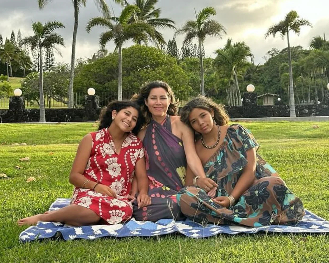 Three women wearing modern mu'umu'u dresses with Hawaiian prints sitting on grass outdoors