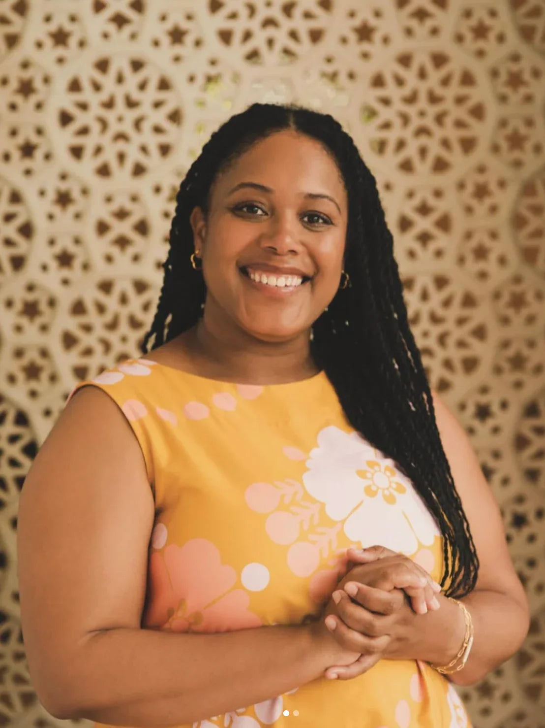 Smiling woman in a yellow floral mu'umu'u dress with an intricate patterned background