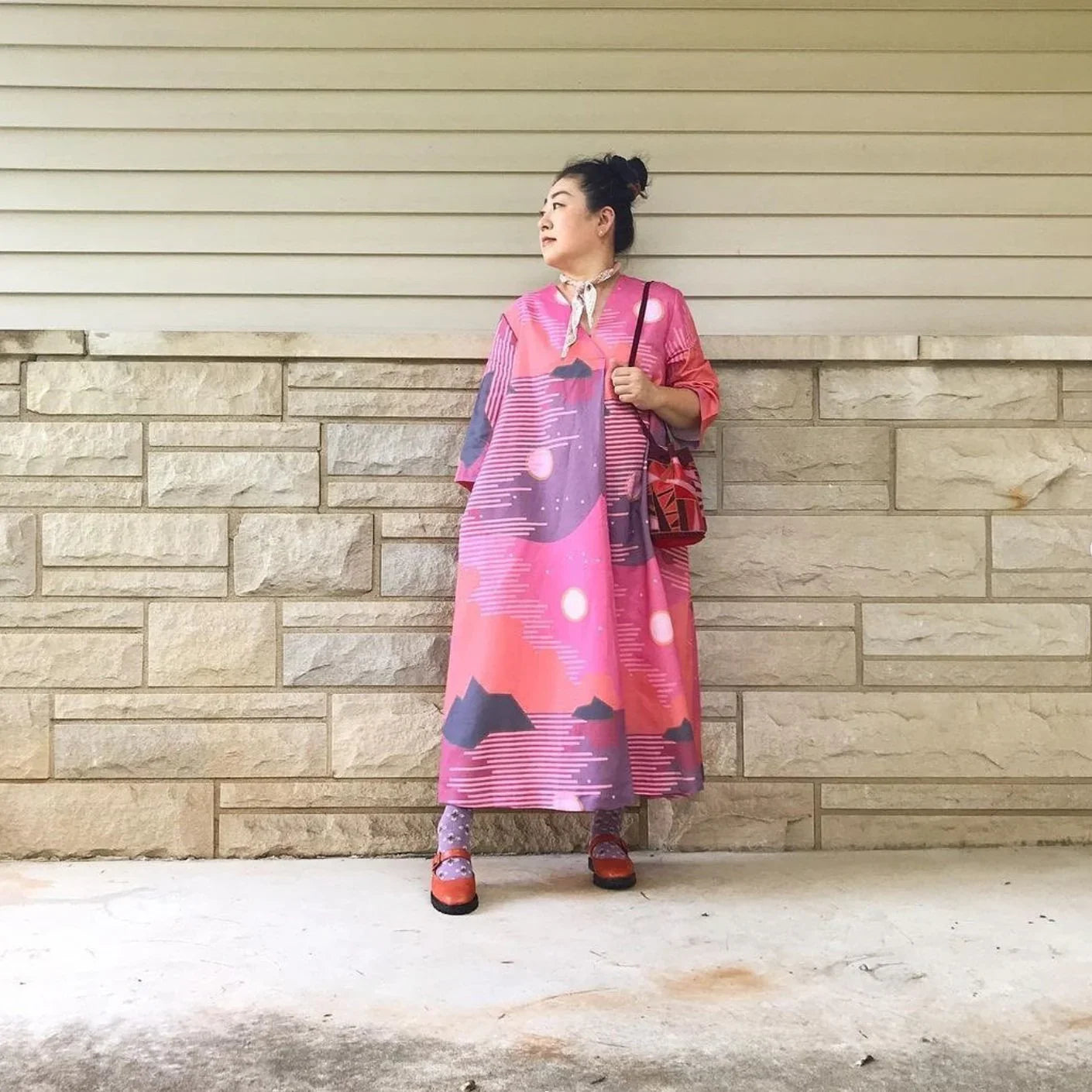 Woman wearing a modern pink mu'umu'u dress with Hawaiian-inspired print, standing outdoors