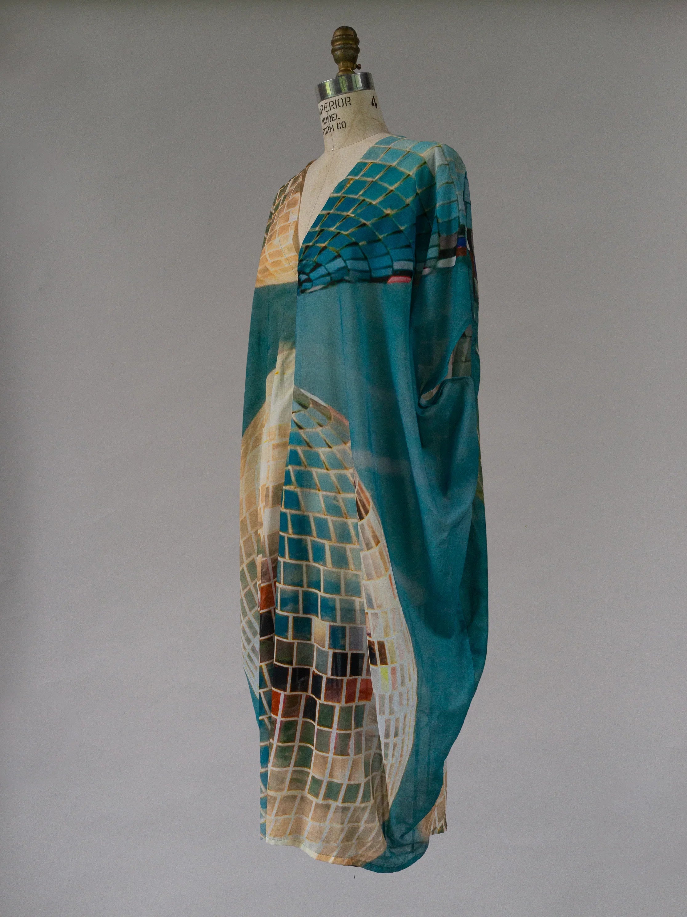 Flowy turquoise kaftan with geometric mosaic print on dress form, modern muumuu style