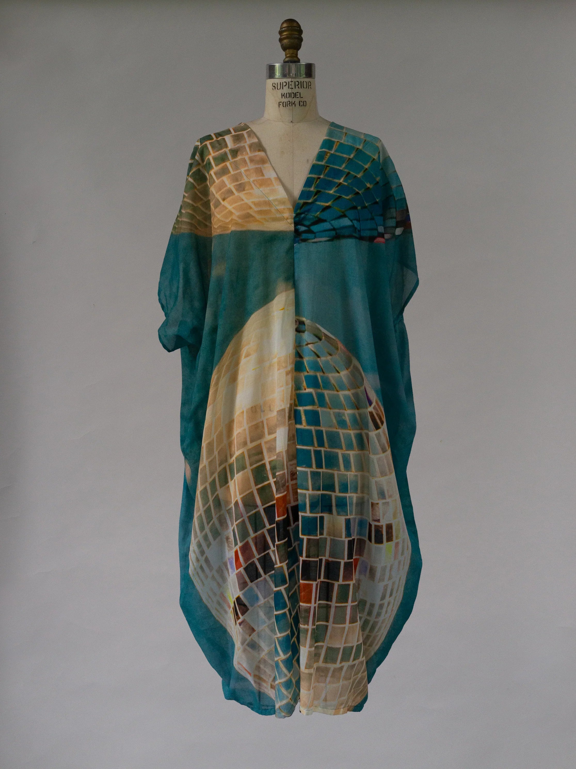 Flowy kaftan dress with abstract mosaic print in teal, beige, and gold tones on mannequin