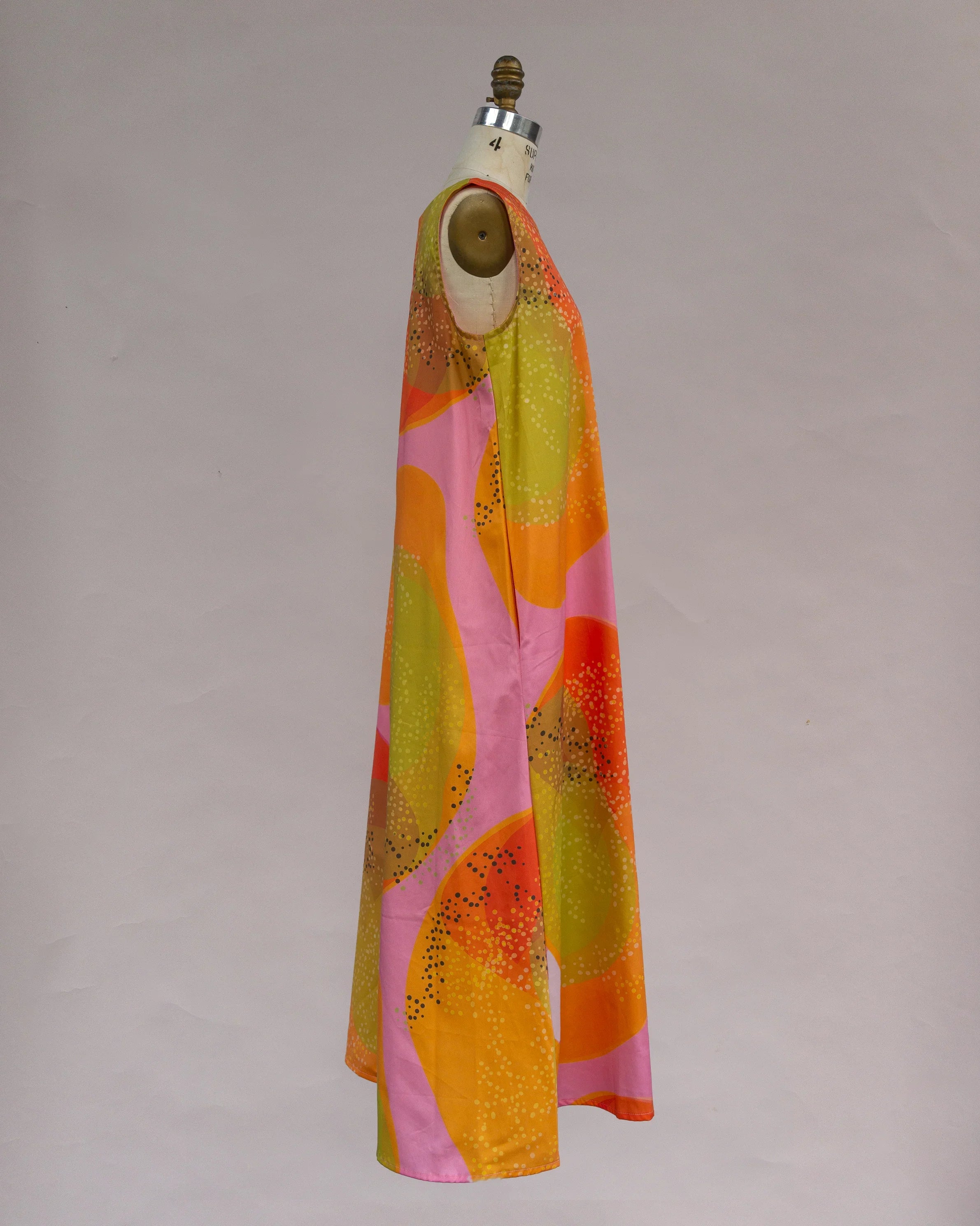 Sleeveless muumuu dress with abstract orange, yellow, and pink Hawaiian print on mannequin